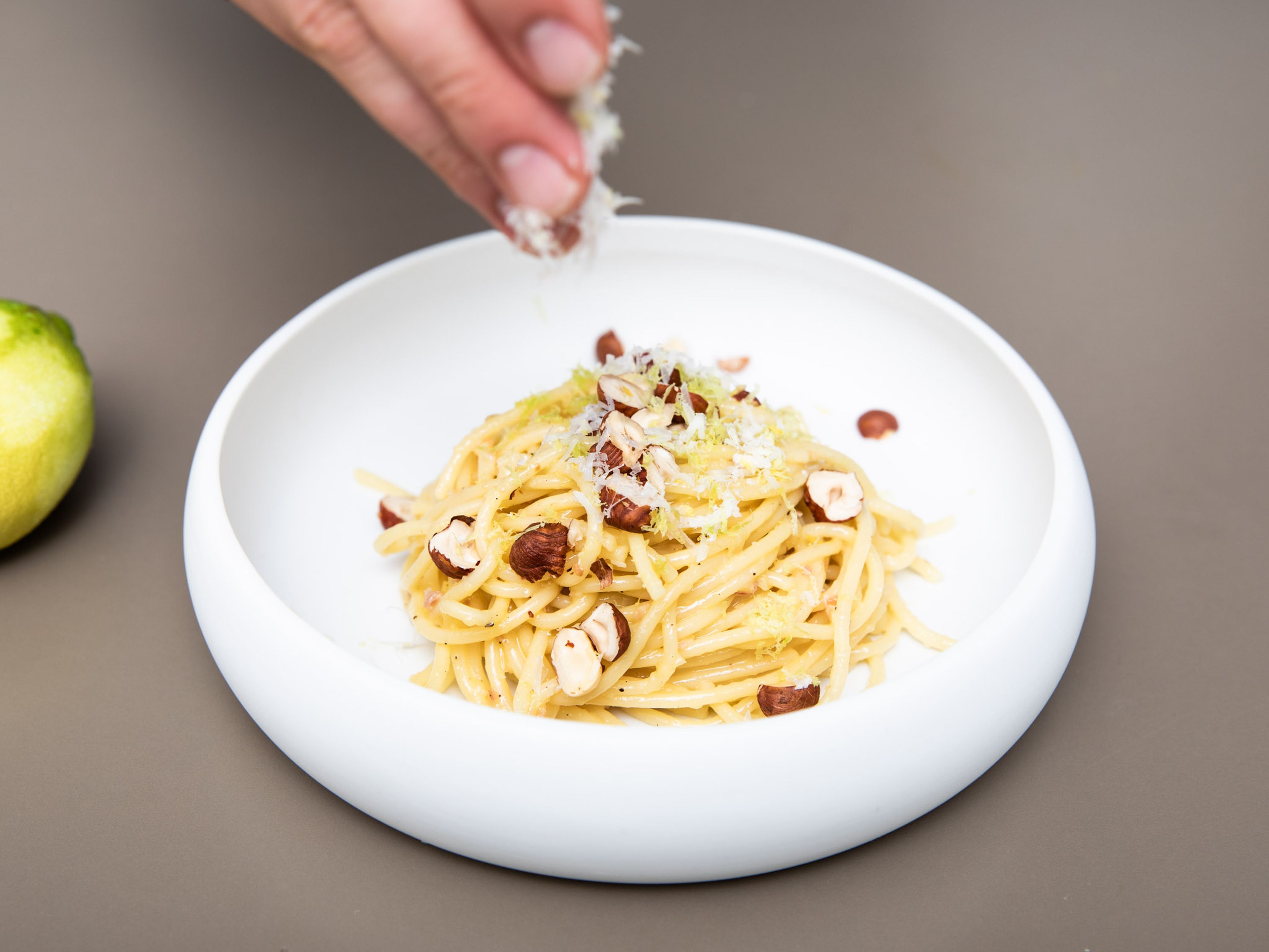 Die Spaghetti Carbonara mit restlichem Zitronenabrieb, gehackten Haselnüssen und nach Wunsch mehr Parmesankäse servieren. Guten Appetit!