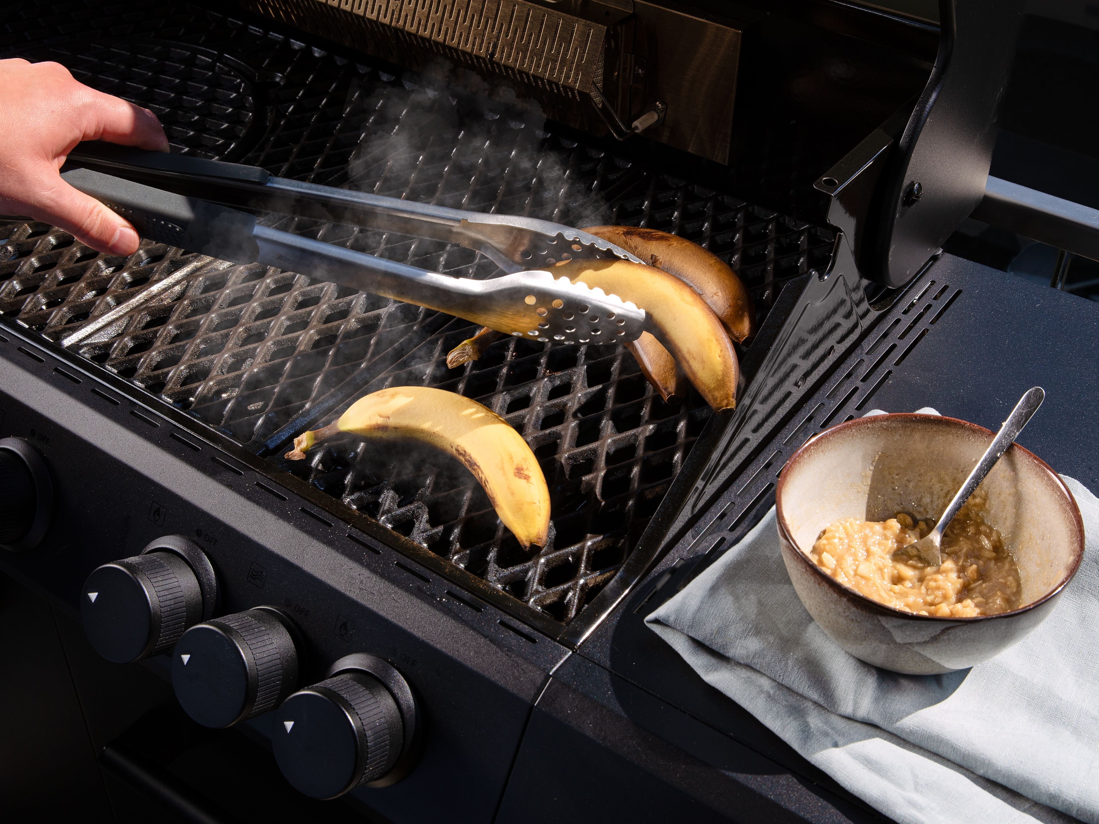 In einer kleinen Schüssel Ahornsirup, Tahini, Kardamom und eine Prise Salz vermischen. Die verbliebenen Macadamianüsse einrühren. Die Bananen in der Schale auf den Grill legen und grillen bis sie ringsherum schwarz und innen weich geworden sind. Zwischendurch mit der Kingstone Grillzange wenden. Anschließend längs aufschneiden und mit der Nussmischung füllen. Für weitere ca. 5 Min. bei geschlossenem Deckel grillen.