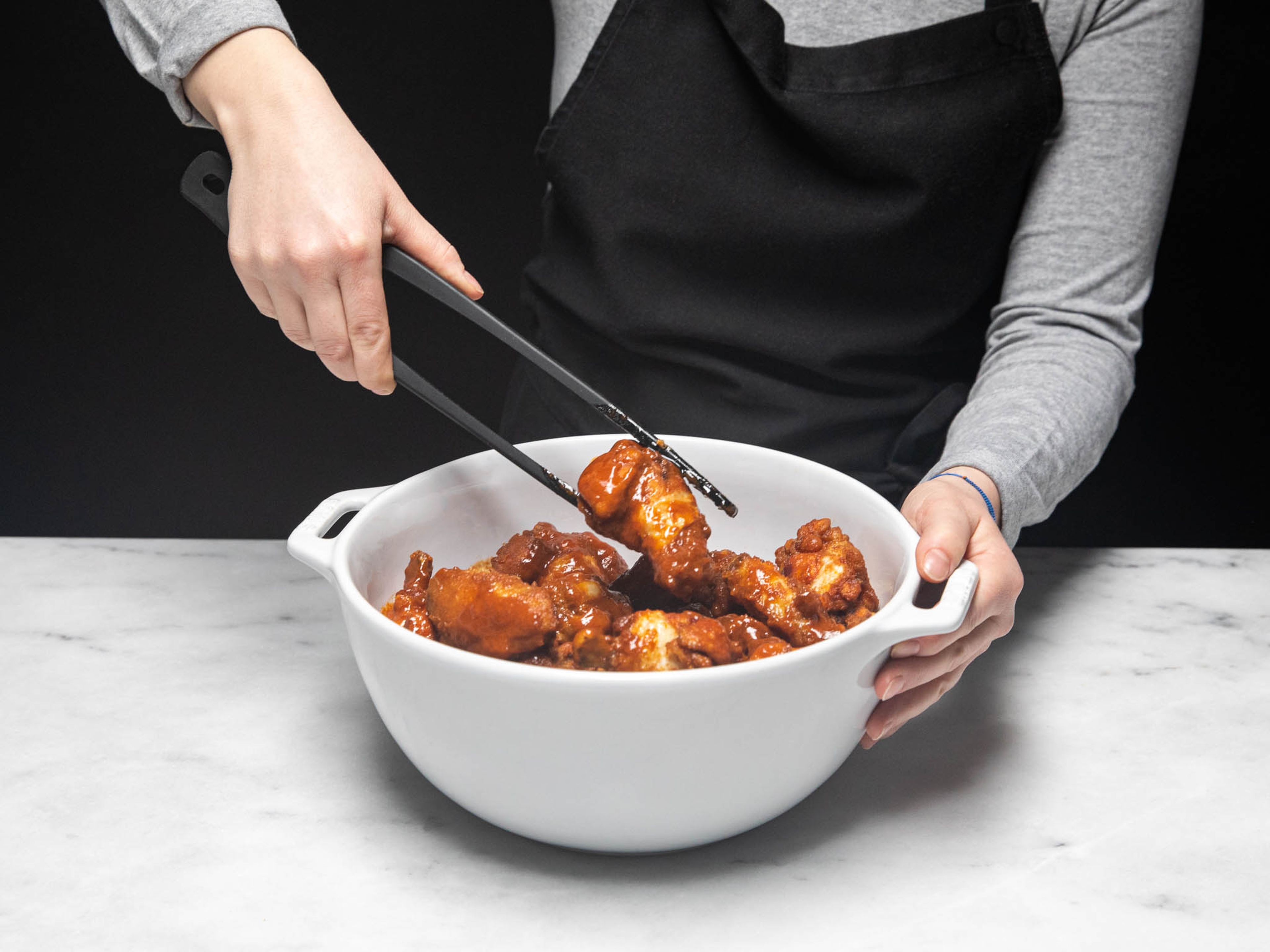 Place the fried wings in a large bowl, pour the red chili sauce on top and toss to coat. Serve on a plate and sprinkle with scallion, chilis, and sesame seeds. Enjoy!