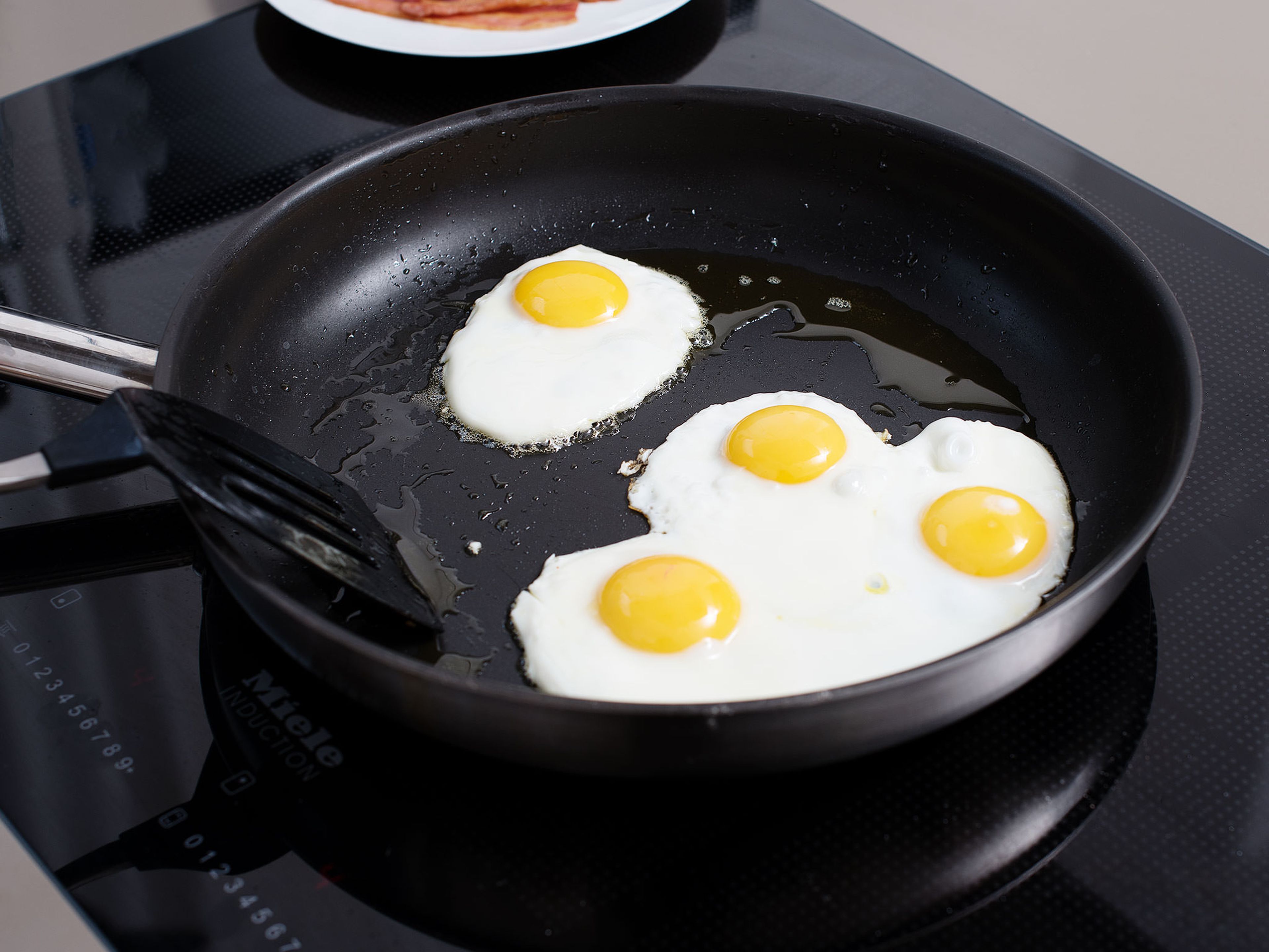 In einer zweiten Pfanne etwas Öl erhitzen und die Eier ca. 3 – 4 Min. zu Spiegeleiern braten. Das Eigelb sollte noch leicht flüssig und die Ränder schön knusprig sein. Mit Salz und Pfeffer abschmecken. Aus der Pfanne nehmen und beiseitestellen.
