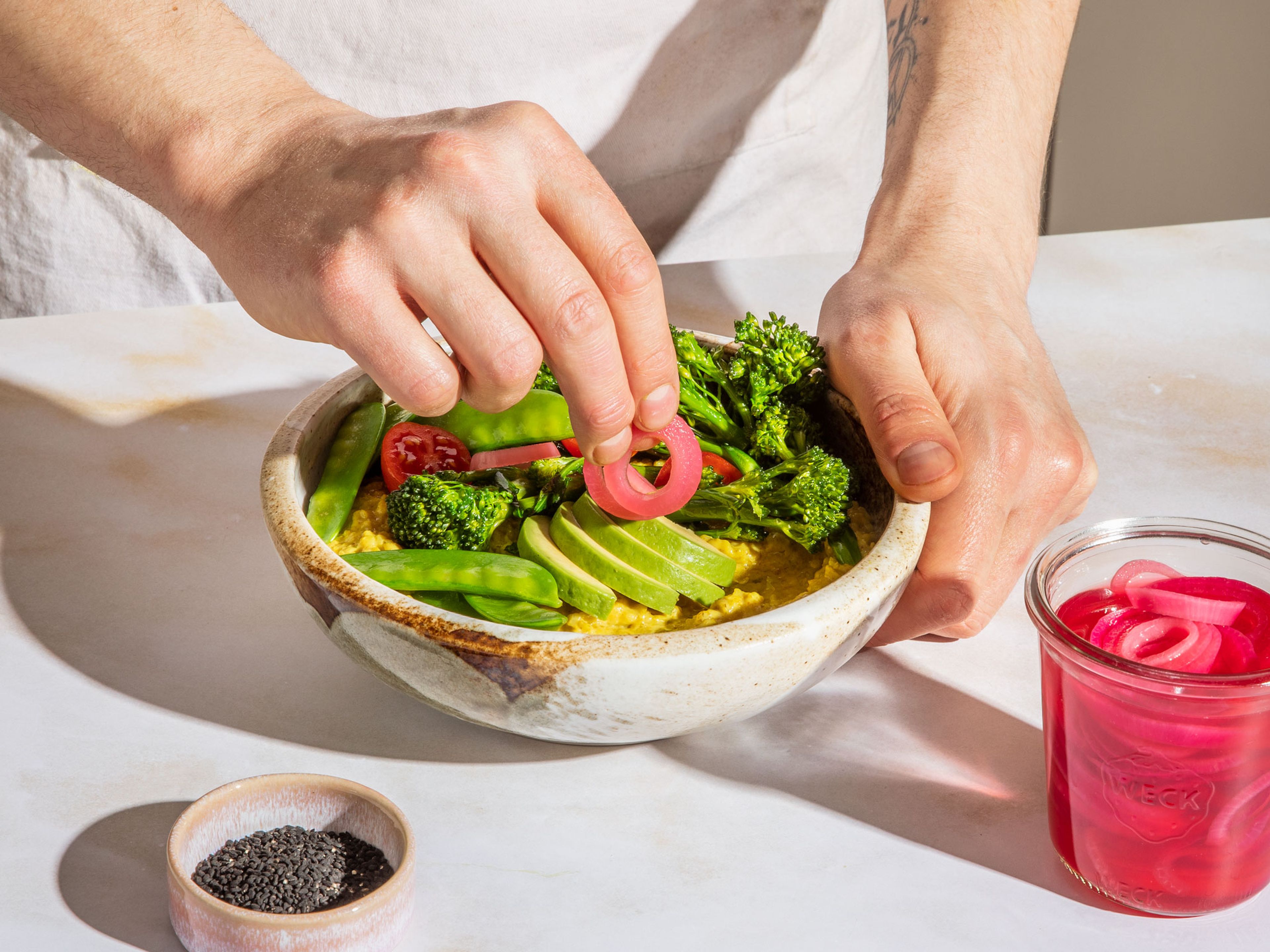 In einer kleinen Schüssel Tahini mit dem Saft einer Limette, etwas Salz und etwas Wasser zu einer zähflüssigen Sauce verrühren. Die Avocado halbieren, Kern entnehmen und die Hälften in Streifen schneiden. Avocado zusammen mit dem anderen Gemüse und eingelegten roten Zwiebeln auf dem Haferbrei anrichten, mit der Tahini-Sauce, Schwarzkümmel und Koriander garnieren.