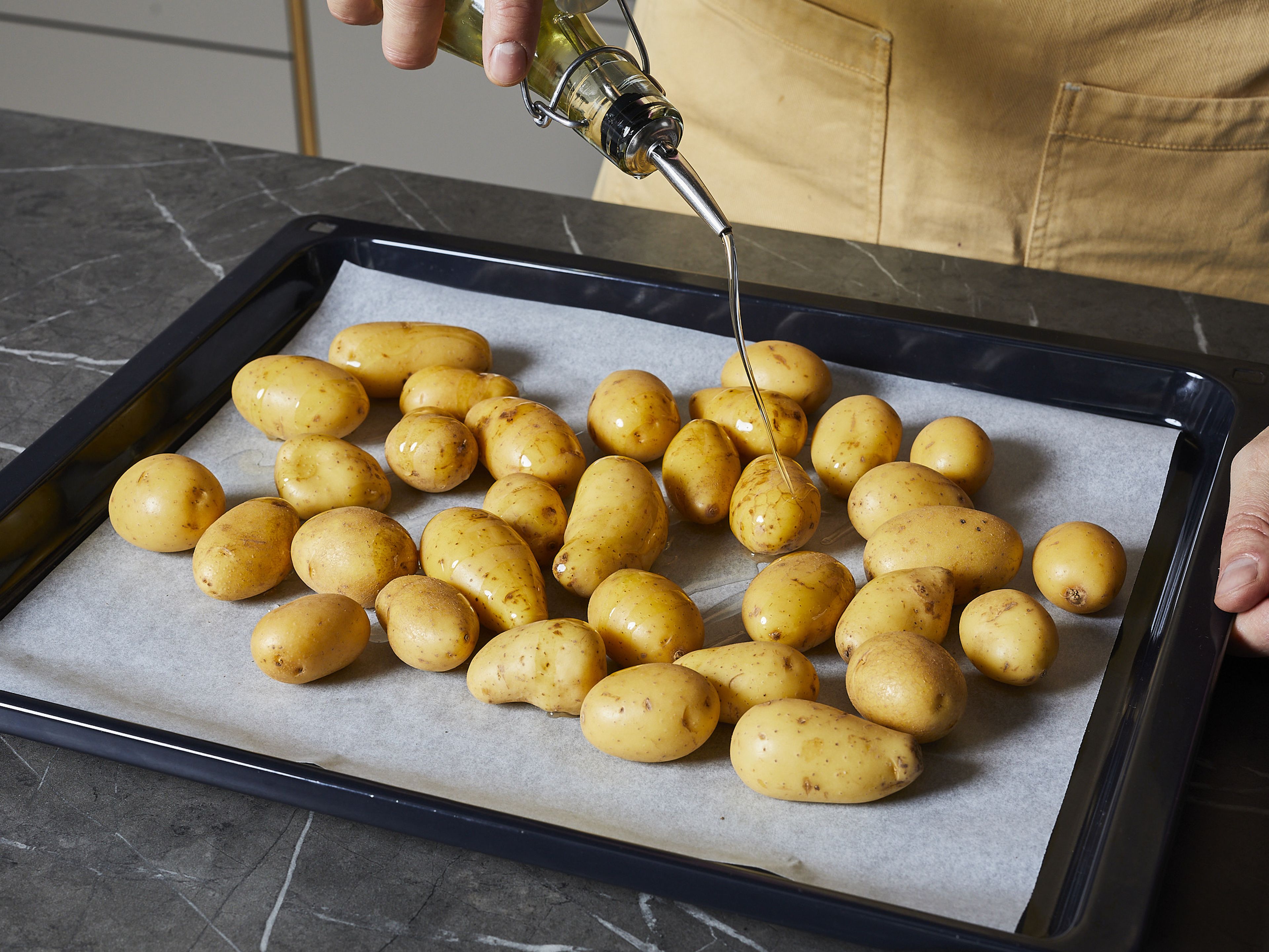 Kartoffeln im Ganzen auf einem mit Backpapier ausgelegten Backblech verteilen und mit ¼ des Olivenöls, Salz und Pfeffer vermischen. Das Backblech in den Ofen geben und ca. 25–30 Min. goldbraun backen. In der Zwischenzeit mit dem Rezept fortfahren.