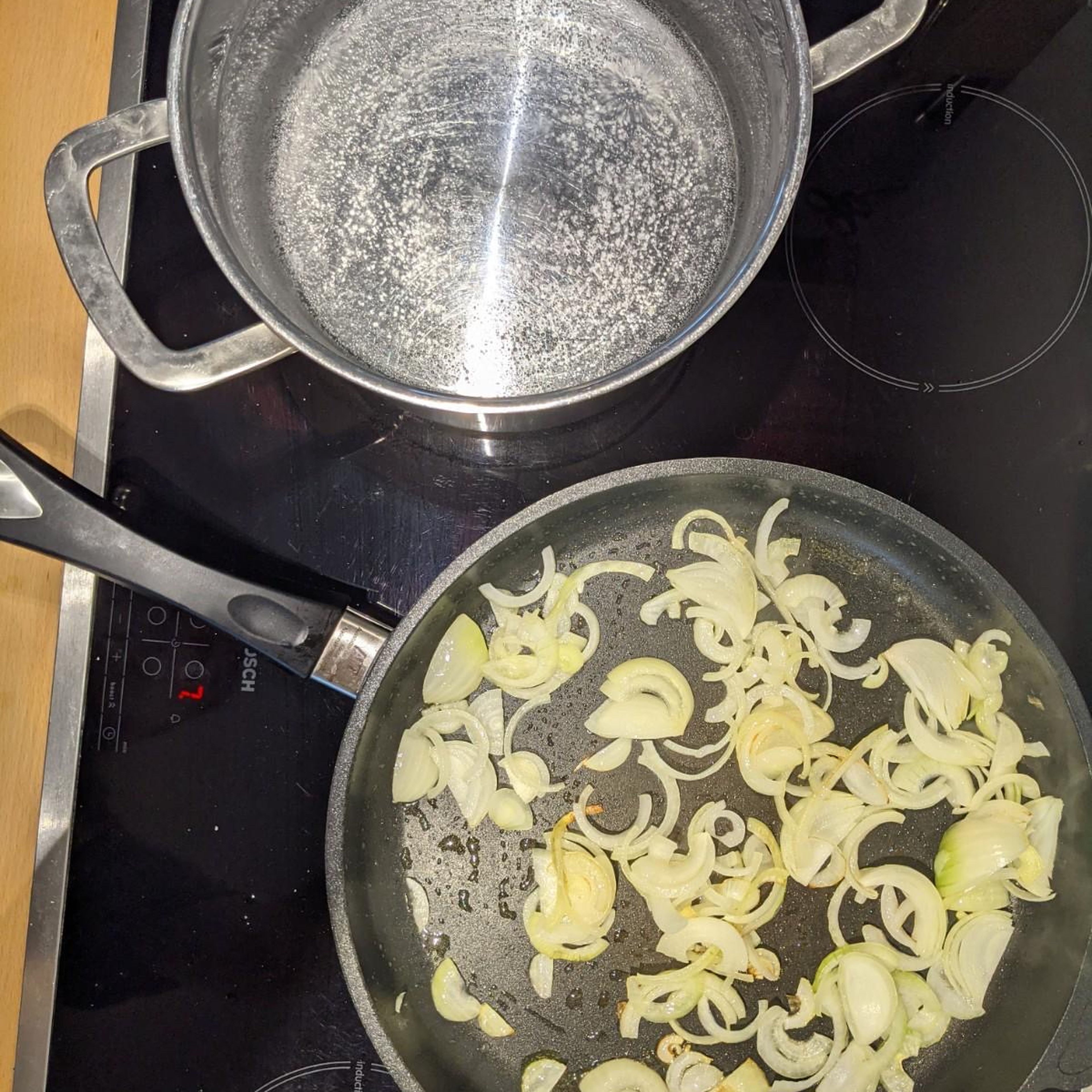 Fange nun an die Zwiebeln zu schneiden und diese dann in einer Pfanne mit etwas Öl zu braten. (Dieser Schritt ist nicht nötig, falls man keine Zwiebeln mag. Währenddessen kannst du anfangen in einem großen Topf Wasser zu kochen und 2 gehäufte TL Salz hinzugeben.