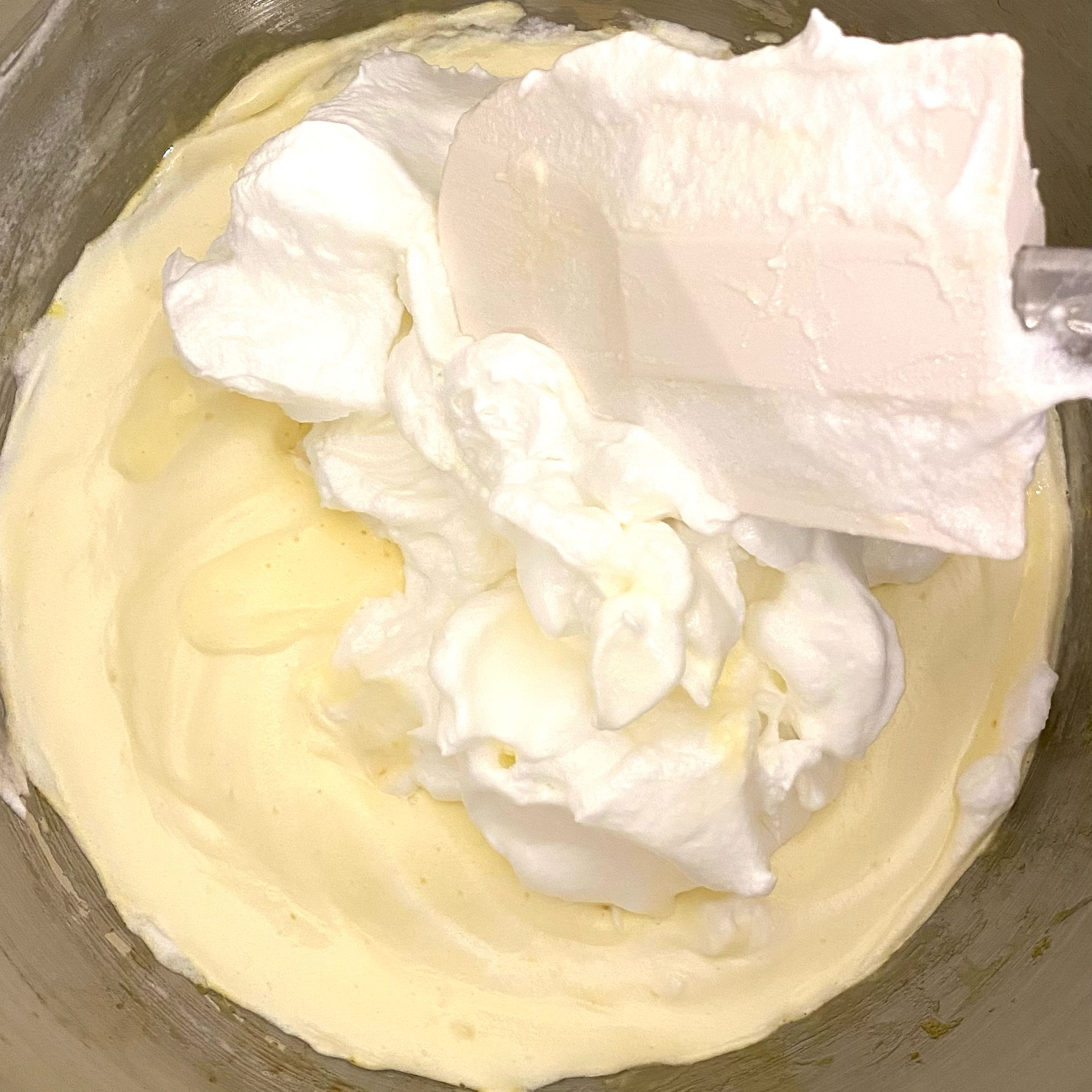 While the stand mixer is running, prepare the meringue: Add egg whites into a separate mixing bowl. Using a hand mixer (unless you have another stand mixer), Let it whisk until the meringue reaches stiff peak, gradually adding the remaining half (about 100gram) of the sugar. Add half of the finished meringue into the ribbon staged yolk mixture, folding gently. Fold the remaining meringue into the lightened yolk mixture very carefully, try your best not to deflate the batter. 

