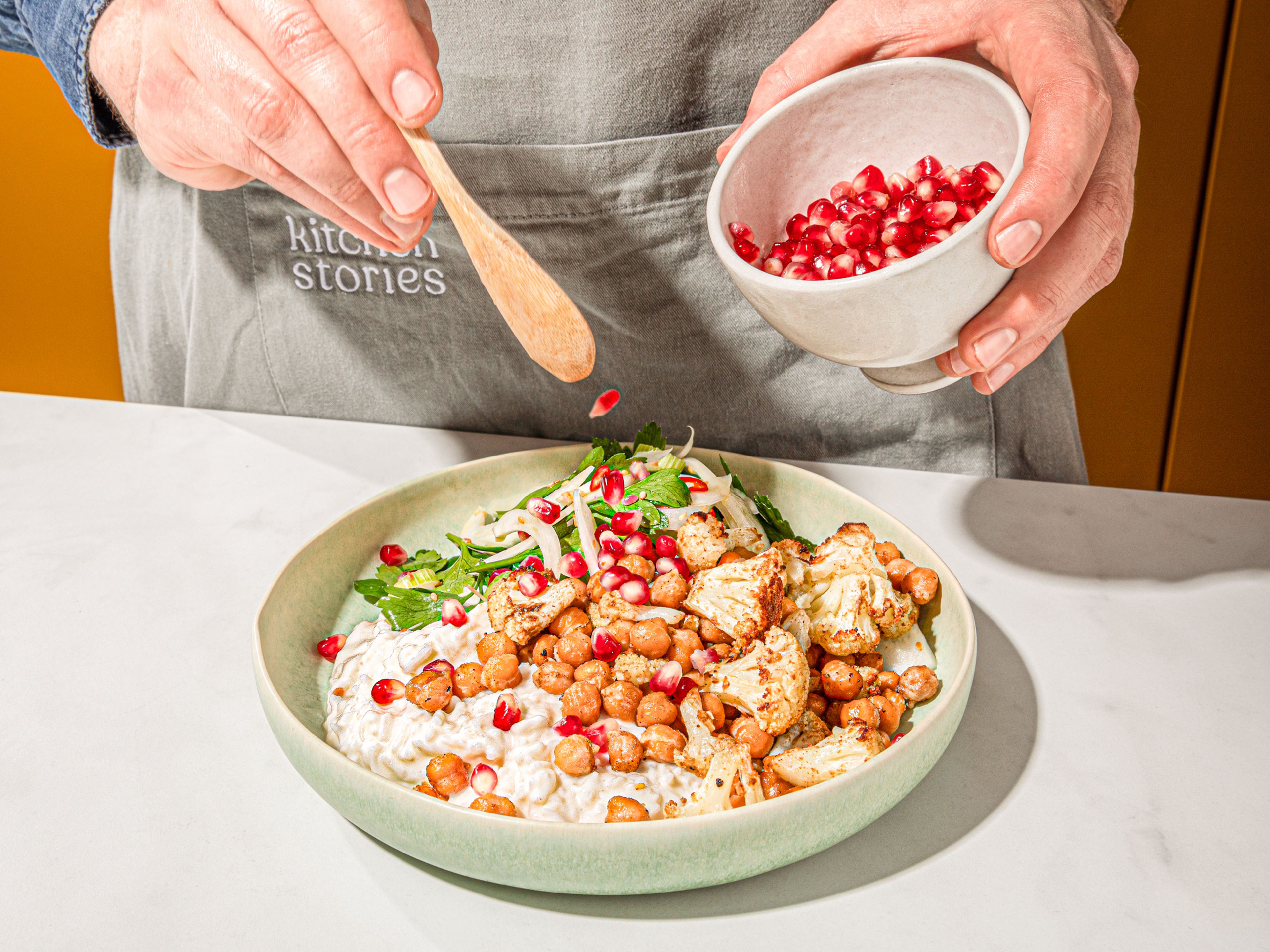 Geröstete Kichererbsen, Blumenkohl, Fenchelsalat und Lughurtreis auf Tellern anrichten und mit Granatapfelkernen bestreuen.