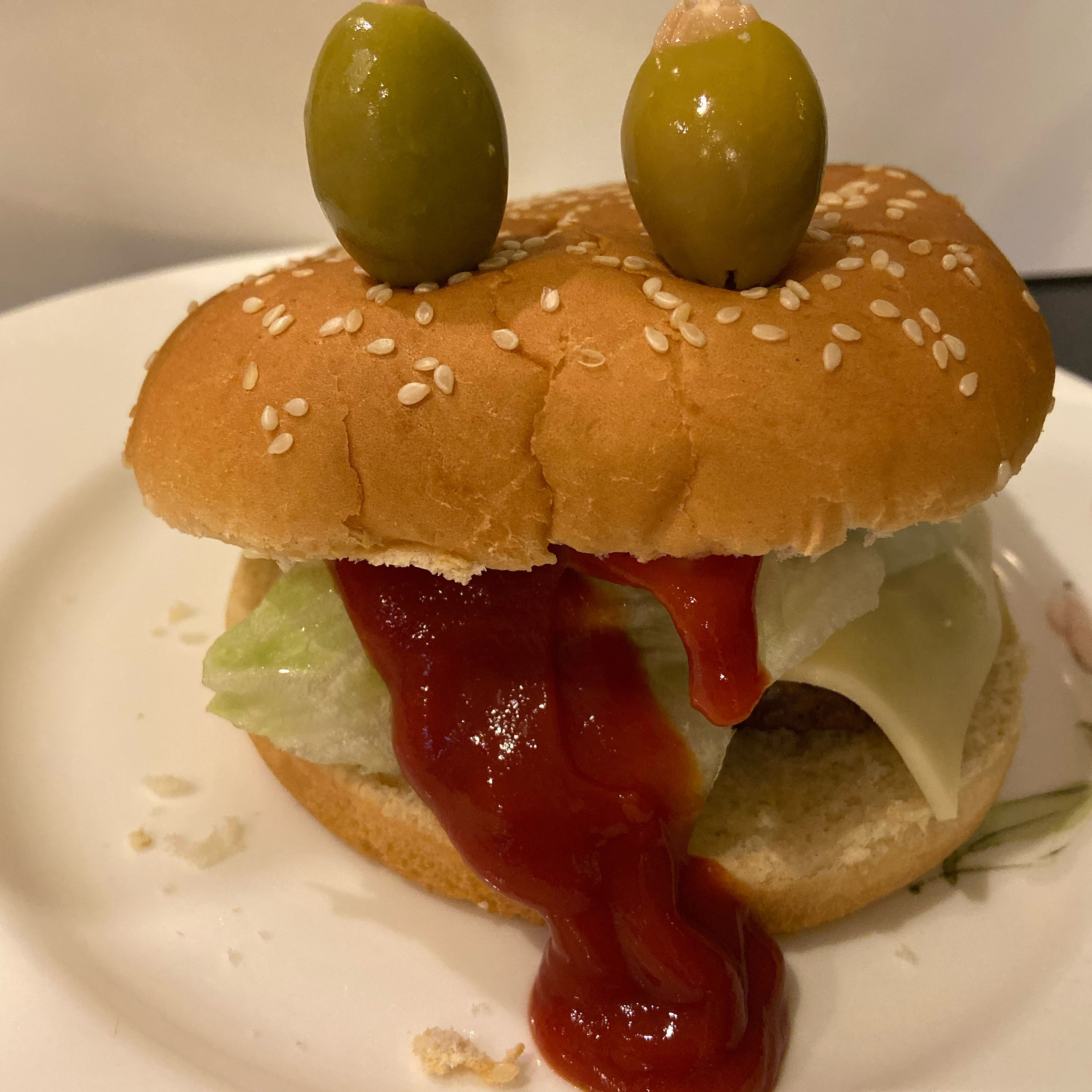 Jedes Burgerbrötchen mit Fleisch, Gemüse und Käse befüllen. Danach jeweils zwei Oliven aufspießen oben auf den Burger spießen. Zum Schluss viel Ketchup oder Burgersoße aus dem Burger herauslaufen lassen.
