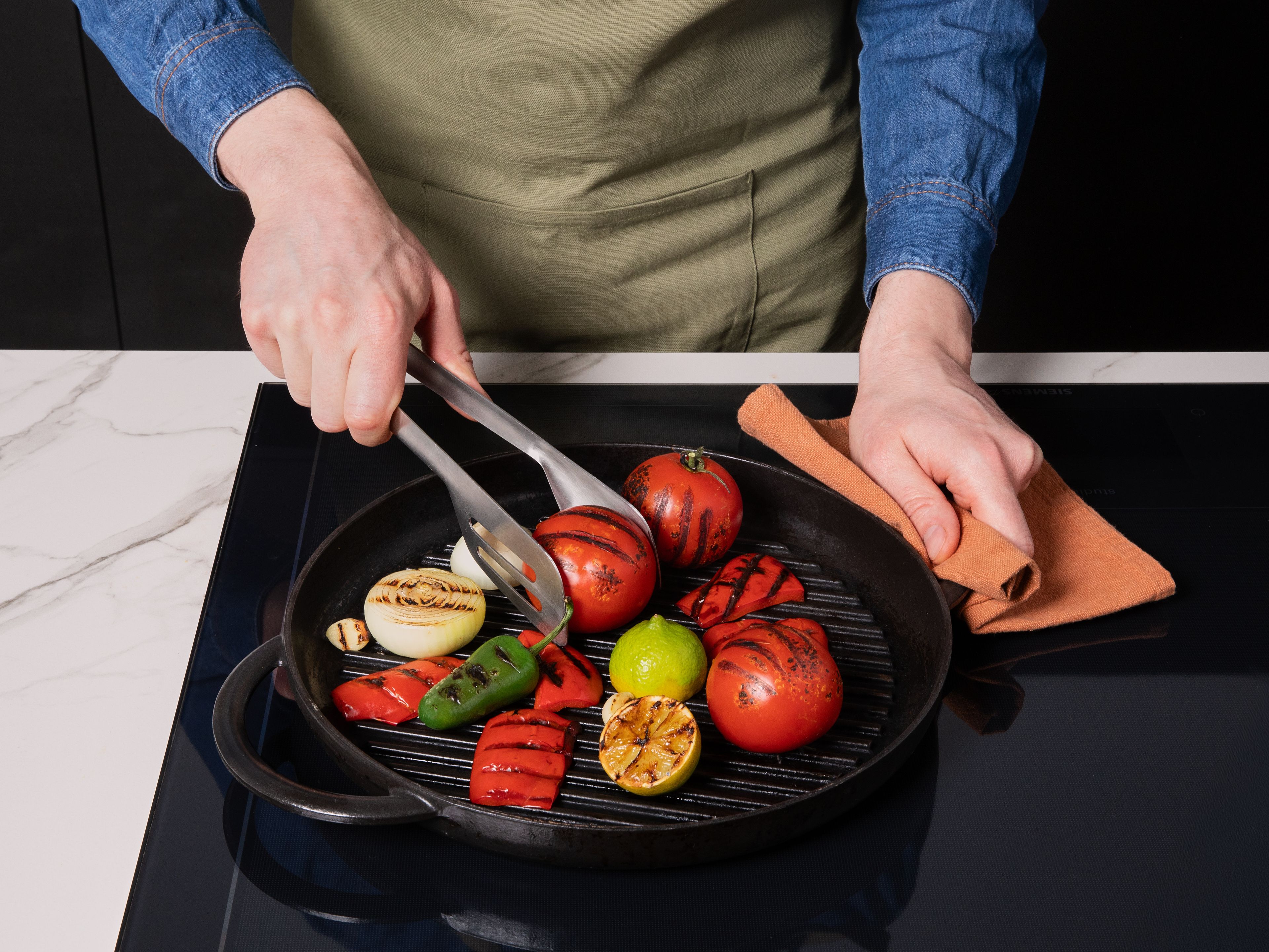 Eine Grillpfanne oder den Grill auf hohe Hitze vorheizen. Zuerst die Salsa vorbereiten: Dafür Zwiebeln schälen und halbieren. Paprika halbieren, entkernen und Strunk entfernen. Knoblauch schälen und Limette vierteln. Dann ganze Tomaten, Zwiebel- und Paprikahälften, Knoblauch, Limettenspalten und grüne Chili auf dem Grill oder in einer Grillpfanne rundherum für ca. 3-4 Min. grillen, bis das Gemüse viele dunkle Stellen hat. Alles beiseitestellen und abkühlen lassen.