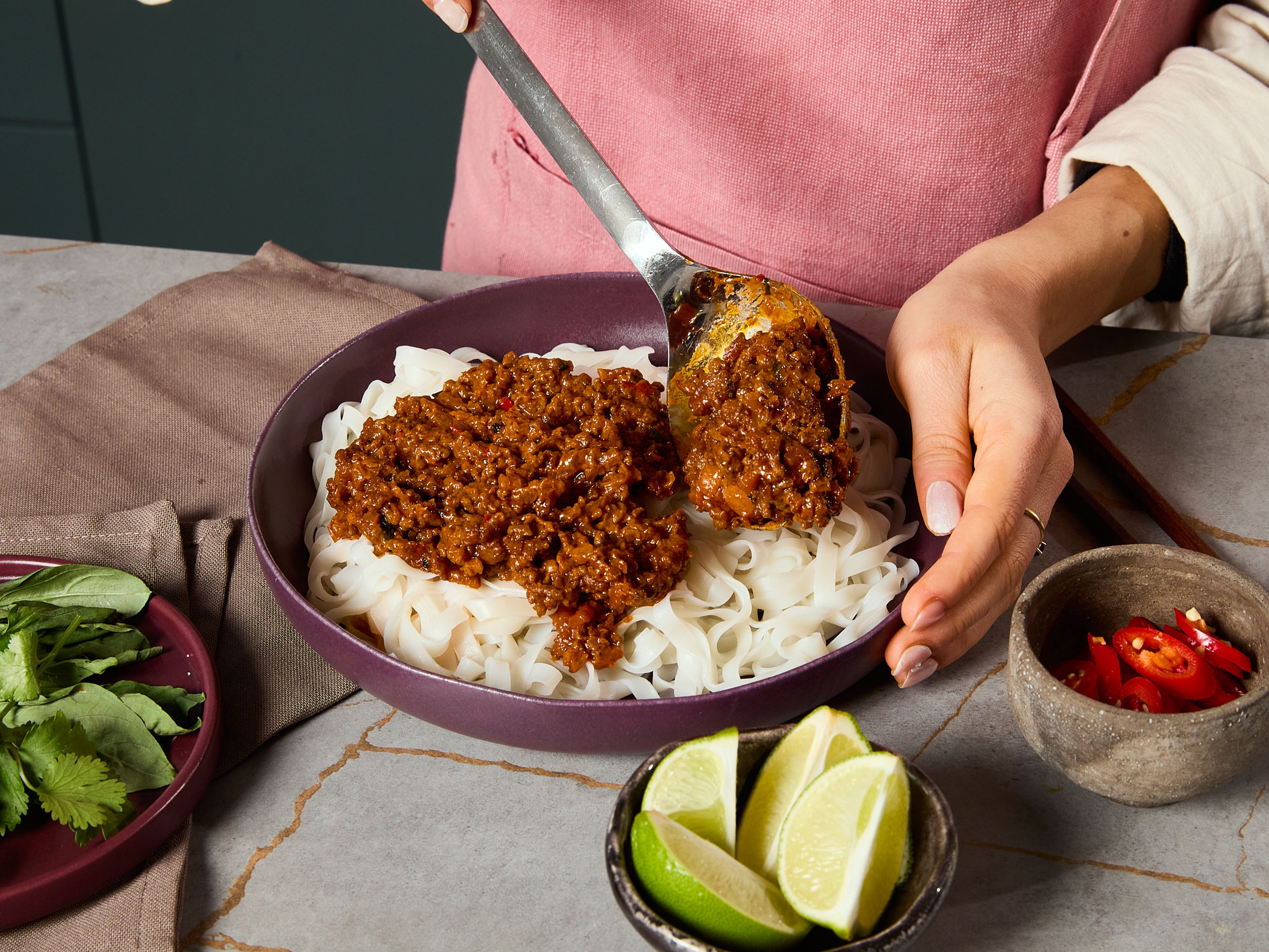 Meanwhile, prepare the rice noodles according to package directions in boiling water, then drain in a sieve. Roughly chop the Thai basil and cilantro. Squeeze the lime and stir the juice into the Bolognese just before serving. Arrange the finished noodles on plates and top with the Thai Bolognese. Sprinkle with the chopped herbs and serve.