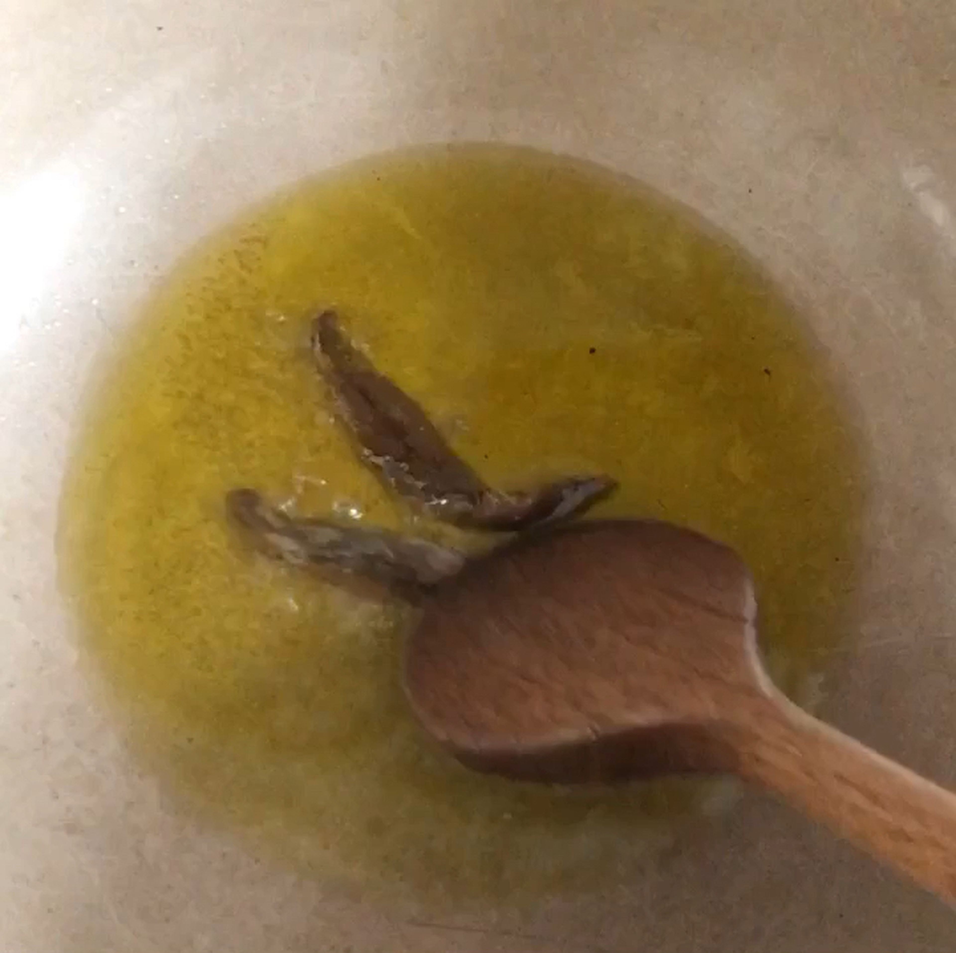 Den Knoblauch mit der Handfläche zerdrücken und die Schale entfernen. Das Olivenöl in einen Topf geben und auf mittlerer Flamme erhitzen. Sardellen hinzufügen, kurz anbraten  und mit einem Holzlöffel zerkleinern.