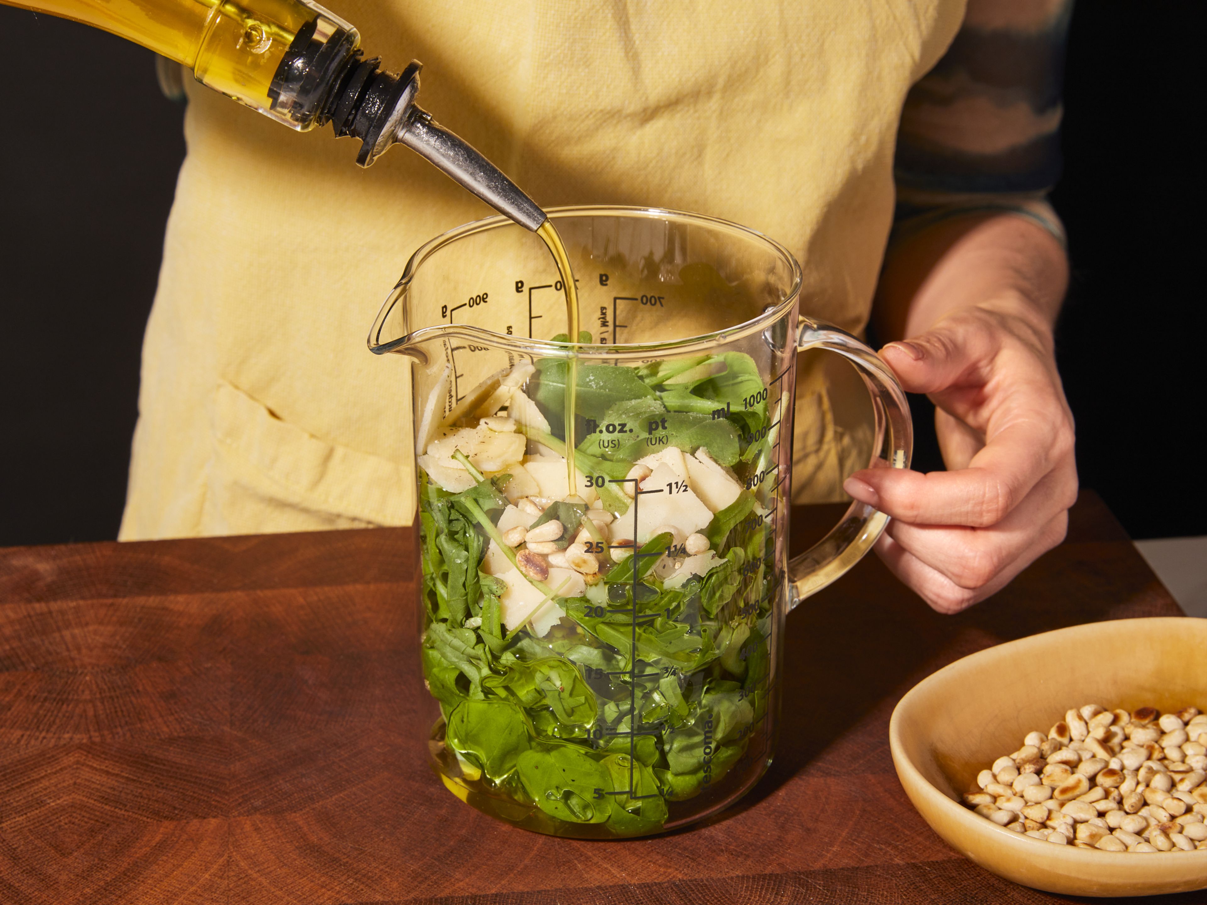 Into the container with garlic cloves, add half of the arugula, basil, ⅓ pine nuts, Parmesan, olive oil, salt, and pepper. Blend with an immersion blender until it’s a smooth pesto. Add water if desired to make it smoother.