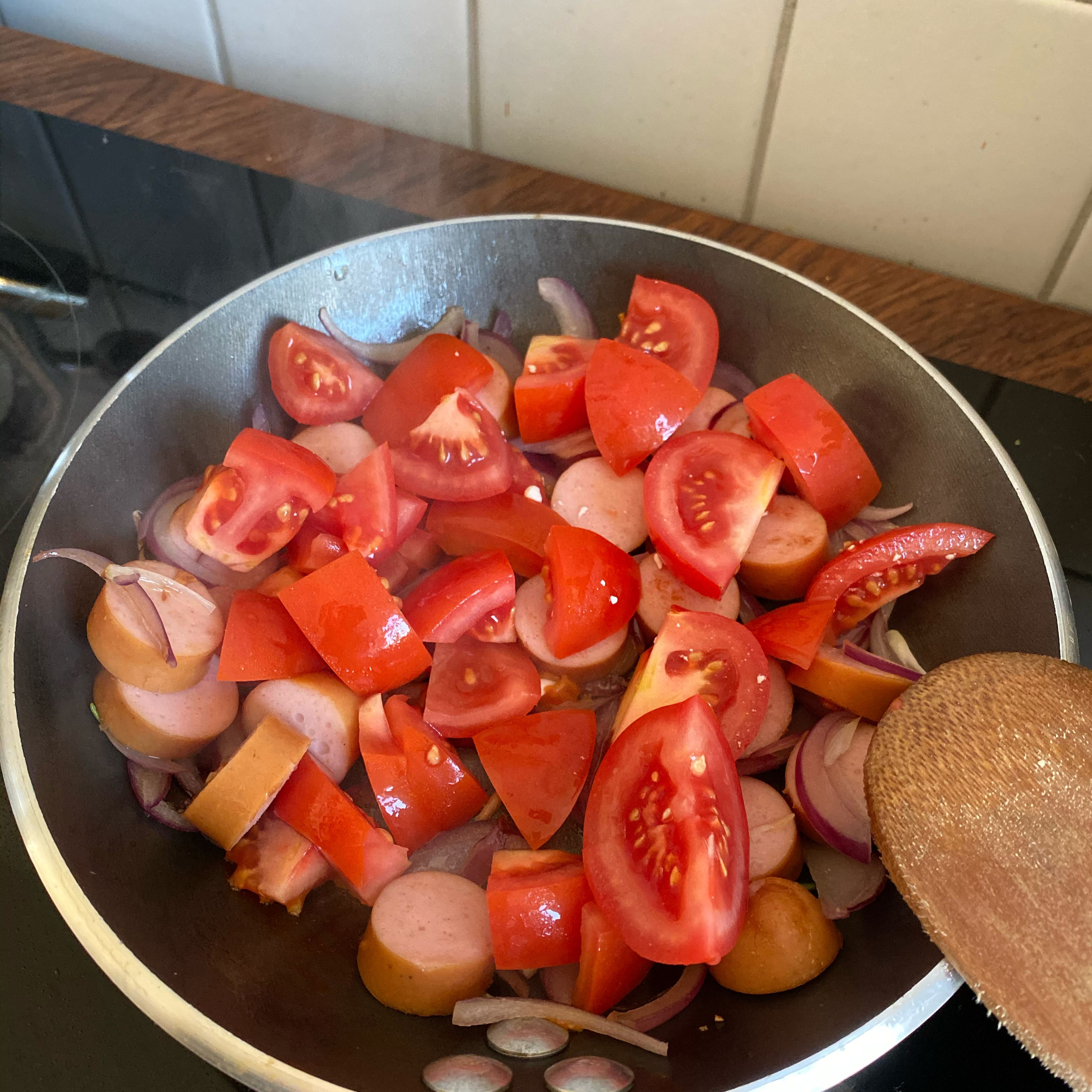 Die Würstchen und die Tomaten in die Pfanne geben und schmoren lassen, bis die Tomaten weich sind.