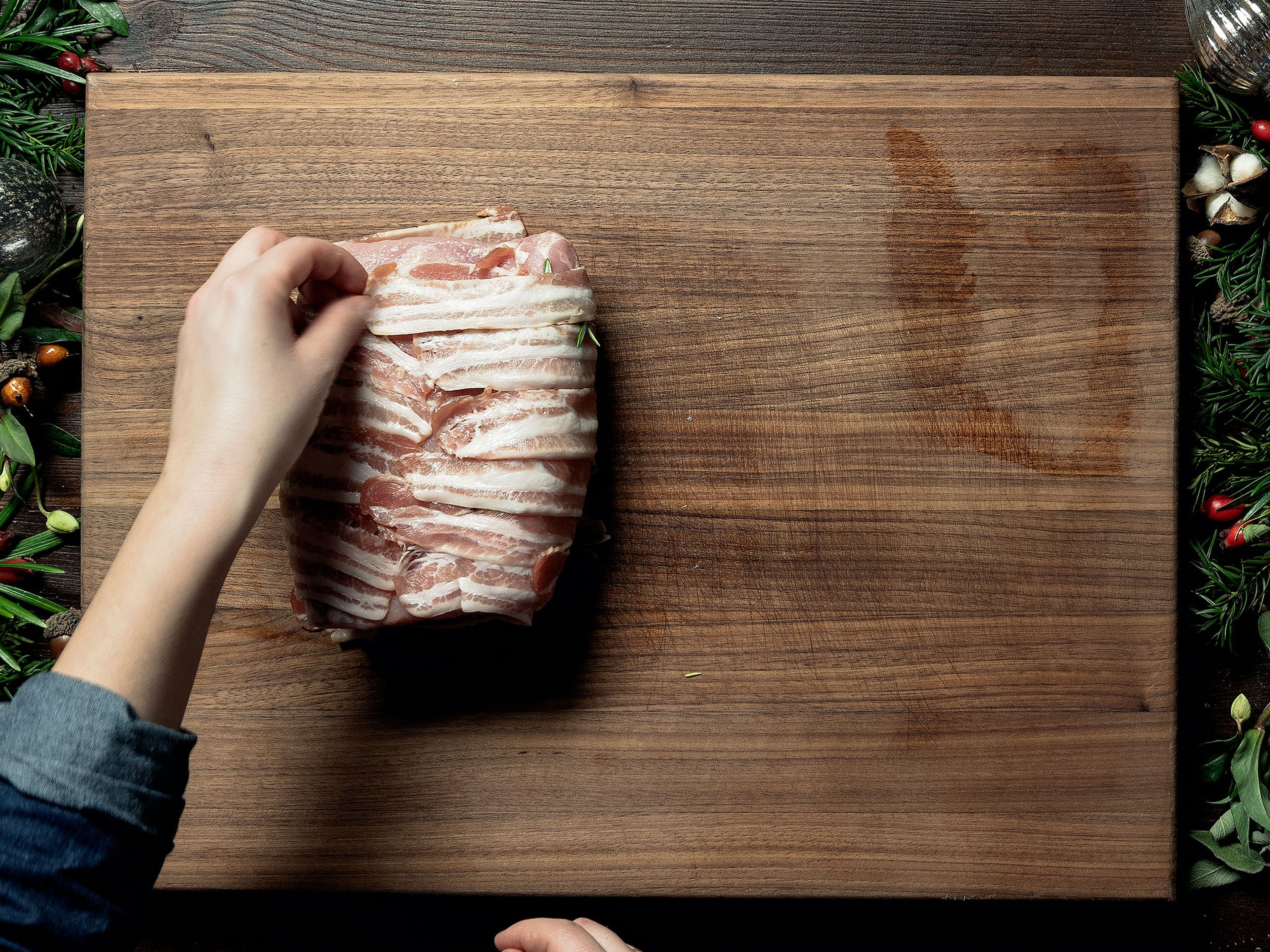 Layer the bacon slices on a work surface. Add rosemary leaves in the middle and add the pork loin, cut side-down. Wrap the bacon around the pork and press together. Tie with kitchen twine.
