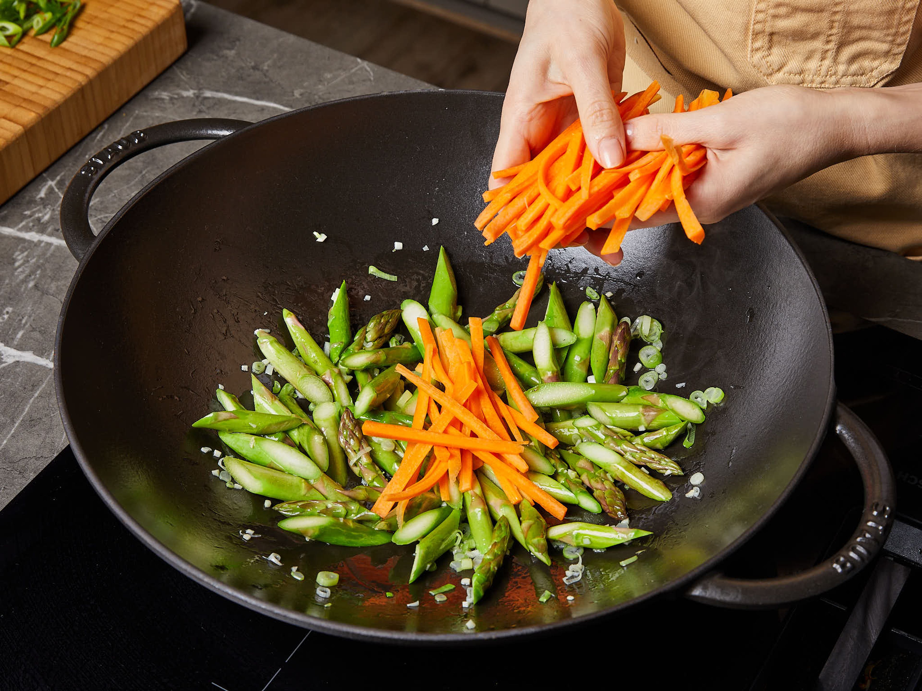 In a heatproof bowl, cover the udons with boiling water. Let them soak for approx. 2 min. until they are loosened. Then drain and set aside or prepare according to package instructions. Heat oil in a large frying pan or wok over medium heat. Add garlic, white part of scallions, and asparagus. Stir-fry for approx. 3 min. over medium heat with chopsticks or a spoon. Then add carrots and continue stir-frying for approx. 3 more min.