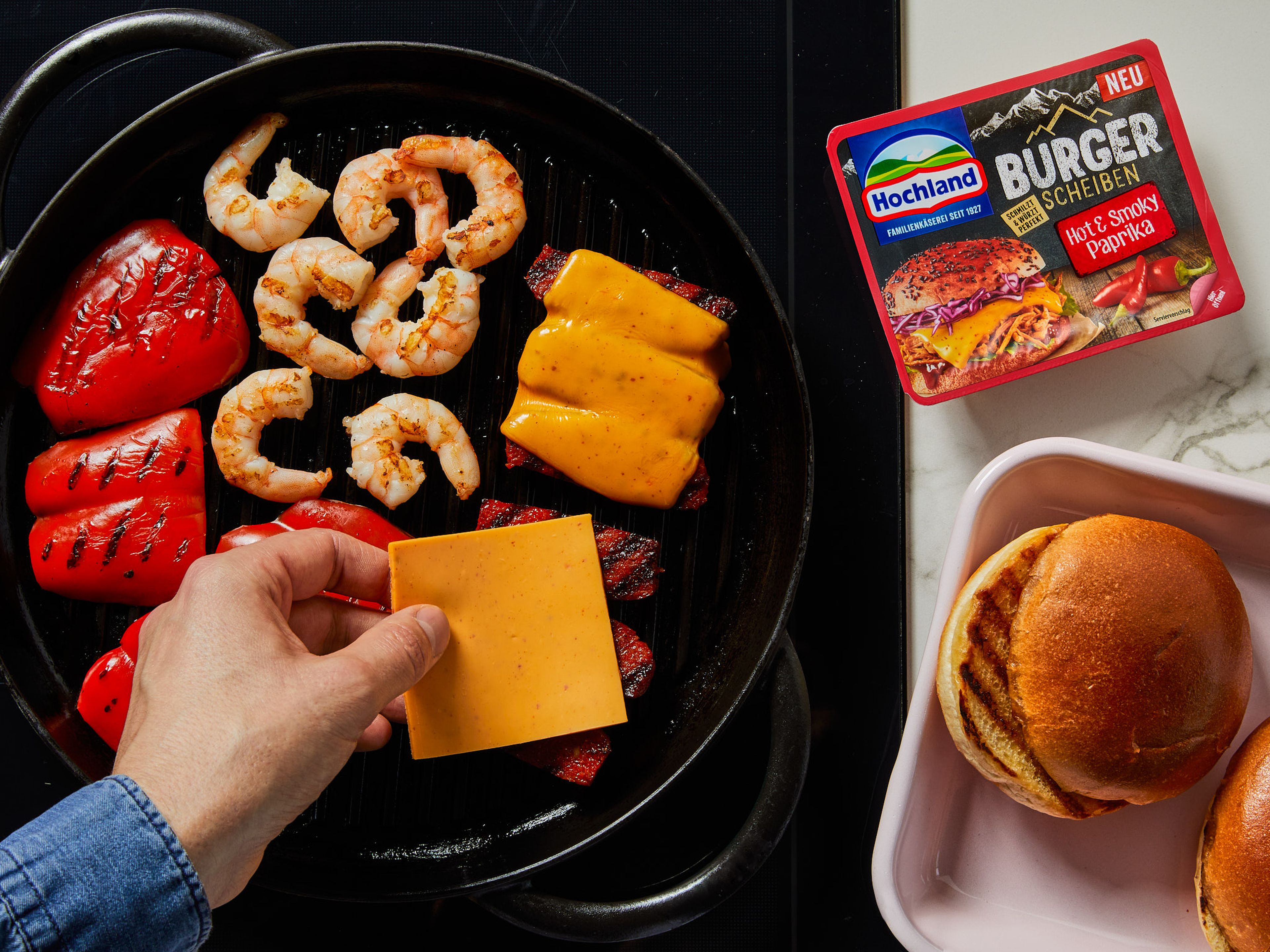 Anschließend Paprikascheiben, Chorizoscheiben und Garnelen auf dem Grill oder in der Grillpfanne garen. Nach ca. 2–3 Min. Paprika, Garnelen und Chorizo wenden und jeweils eine der Hochland Burger Scheiben Hot & Smoky Paprika auf den Chorizoscheiben verteilen.