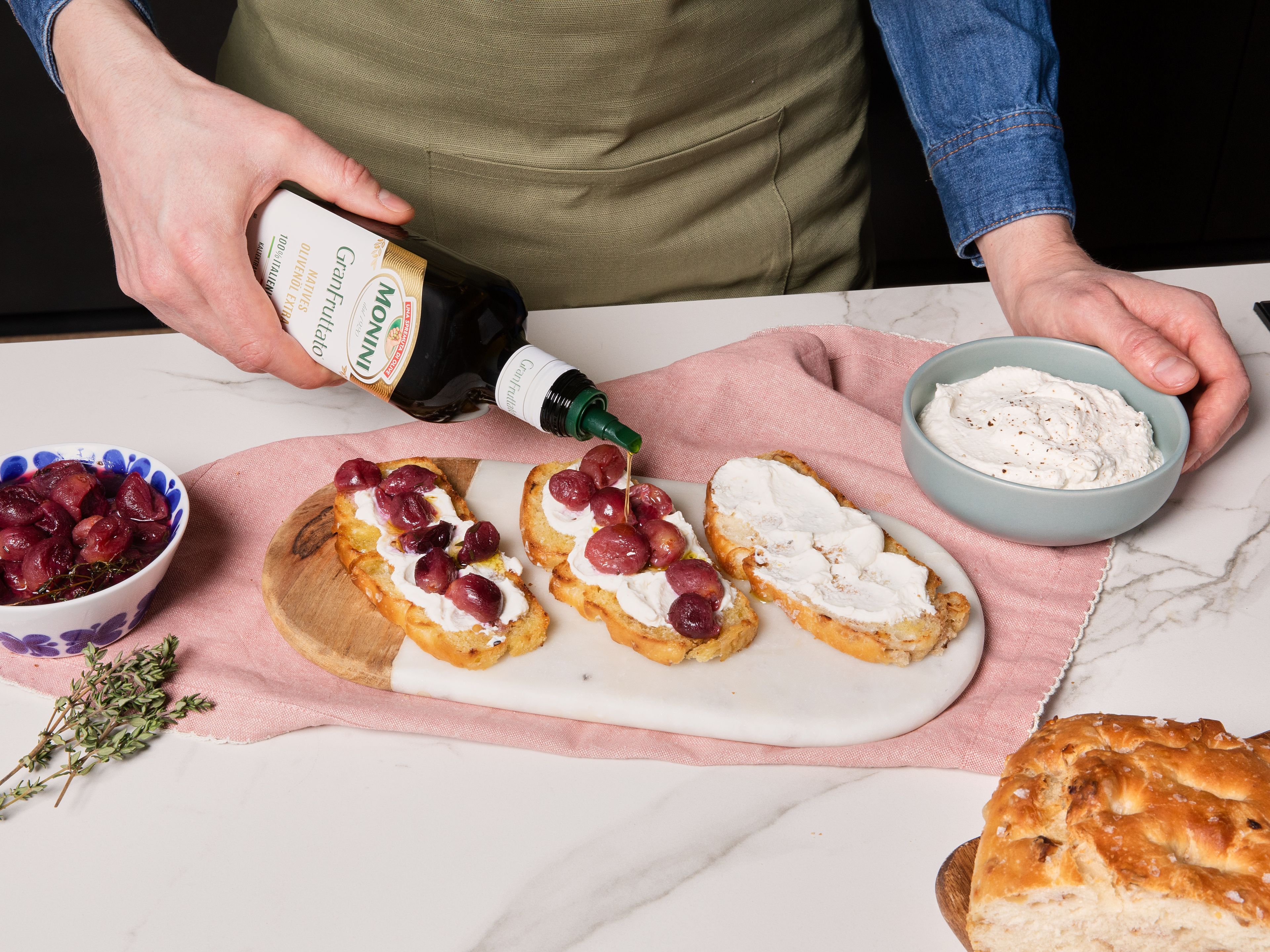 In einer kleinen Schüssel den Ricotta mit Zitronenabrieb vermengen und mit Salz und Pfeffer abschmecken. Nach dem Backen die warme Focaccia leicht abkühlen lassen und in Scheiben schneiden. Mit Zitronen-Ricotta bestreichen, die gerösteten Trauben darauf verteilen und mit Balsamico, Thymianblättchen, Monini GranFruttato und etwas grobem Pfeffer und Meersalz toppen.