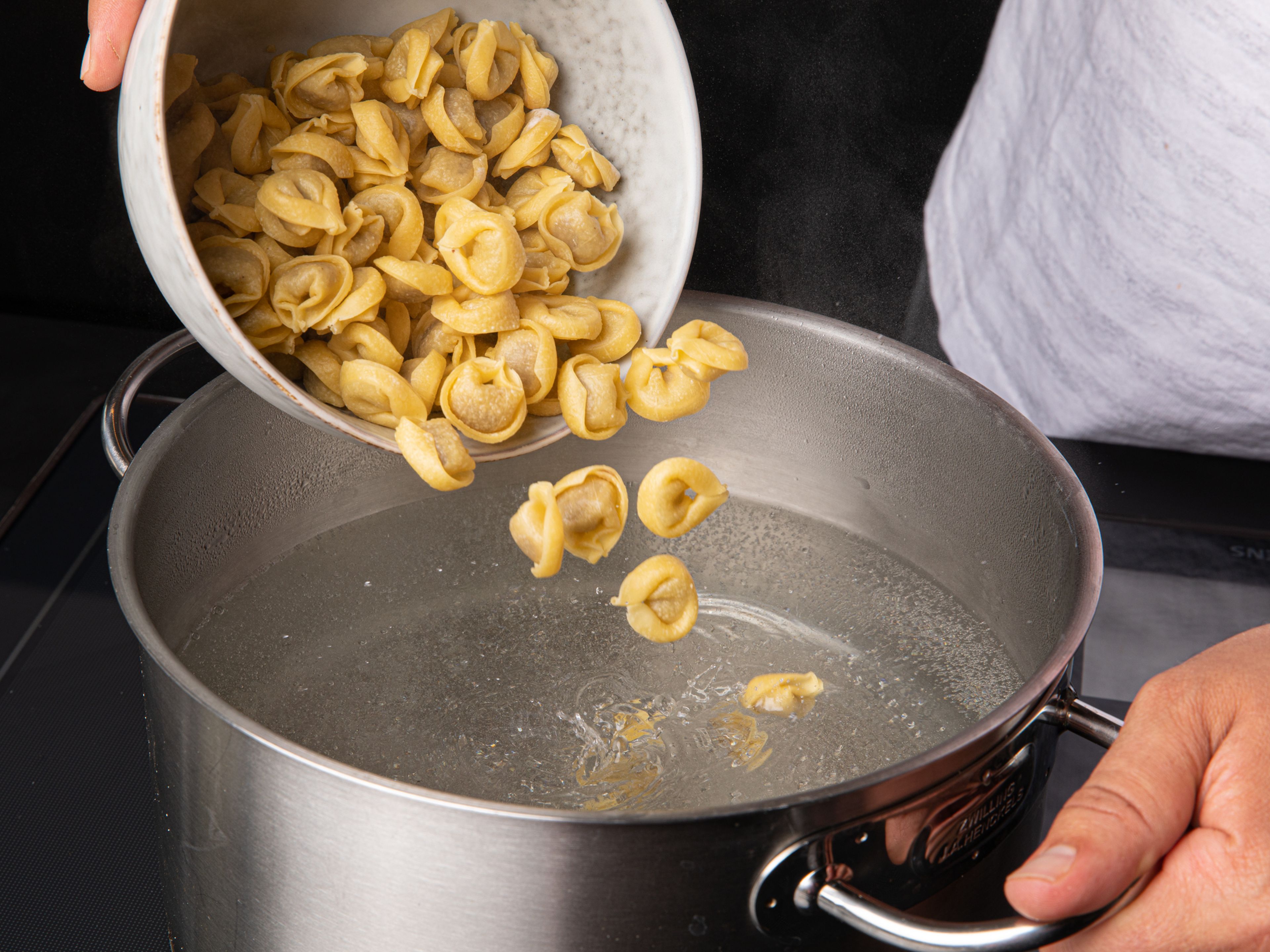 Schinken würfeln und Parmesankäse fein reiben. Einen Topf mit Wasser bei starker Hitze zum Kochen bringen. Großzügig mit Salz würzen und die Tortellini nach Packungsanweisung kochen.