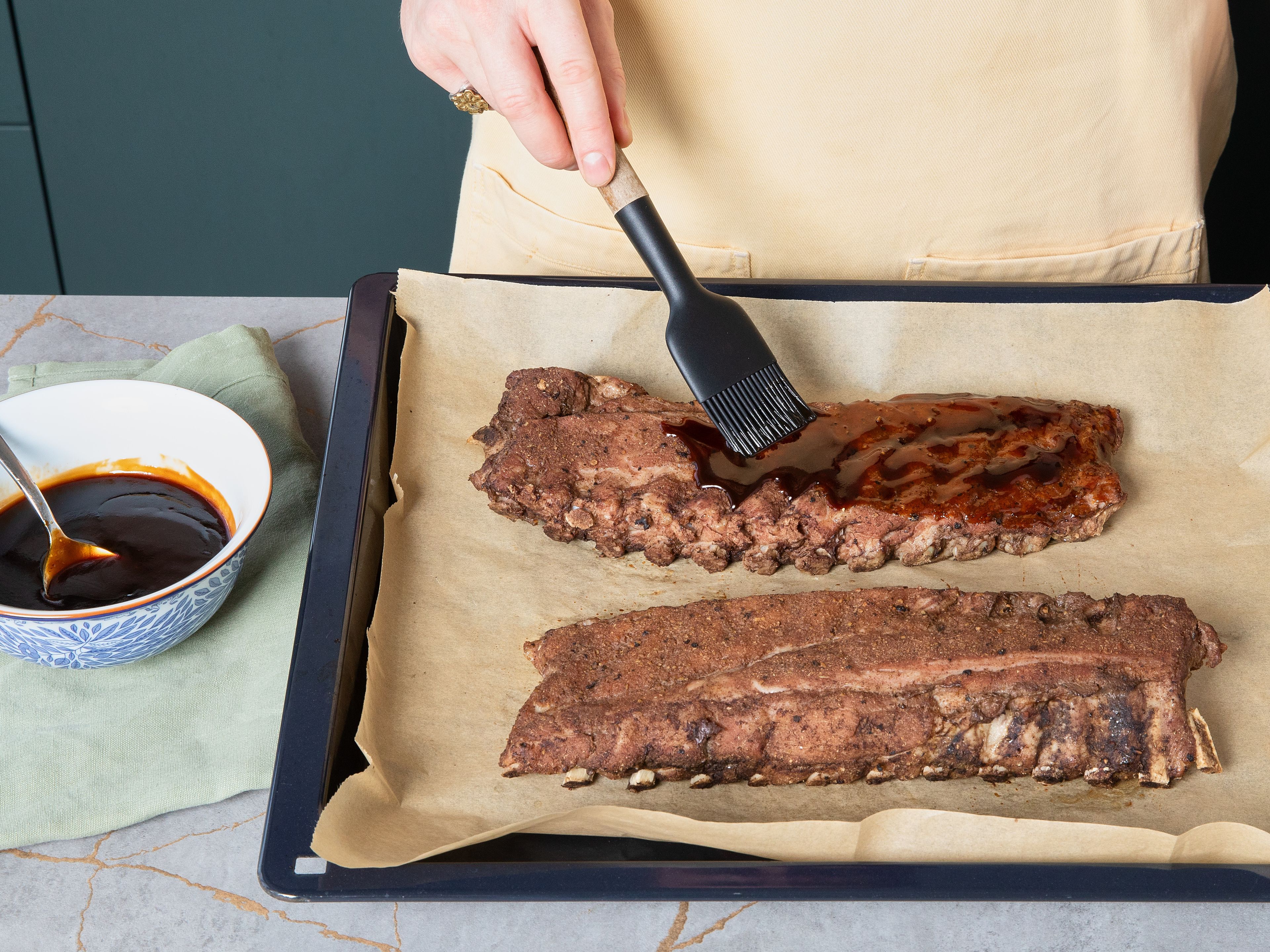 Remove ribs from the oven after approx. 2 hrs. and allow to rest for approx. 15 min. Meanwhile, increase oven temperature to 220°C/428°F. After approx. 15 min., cut open one corner of foil package and pour the excess liquid into a bowl. Remove ribs from foil and place on baking paper, meaty side up. Put tray on the top shelf in oven and bake for approx. 5 min. to form a nice crust. Remove from oven, brush with 2 tbsp sauce, and bake for another approx. 5 min. Remove, add another layer of sauce, and bake for final approx. 5 min. Finally, brush with remaining sauce and garnish with sesame seeds, finely sliced spring onions and some chili, if desired.
