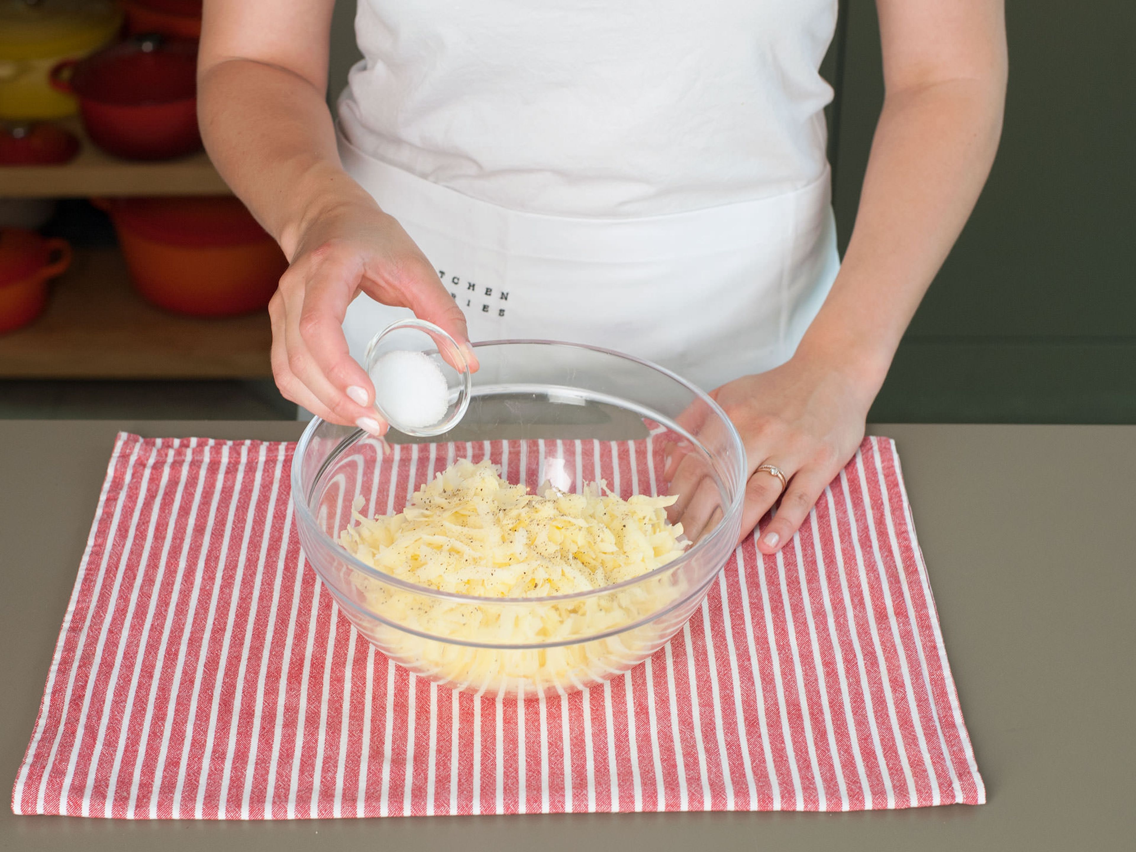 Kartoffelraspeln zurück in die Schüssel geben und mit einer Prise Salz und Pfeffer würzen.