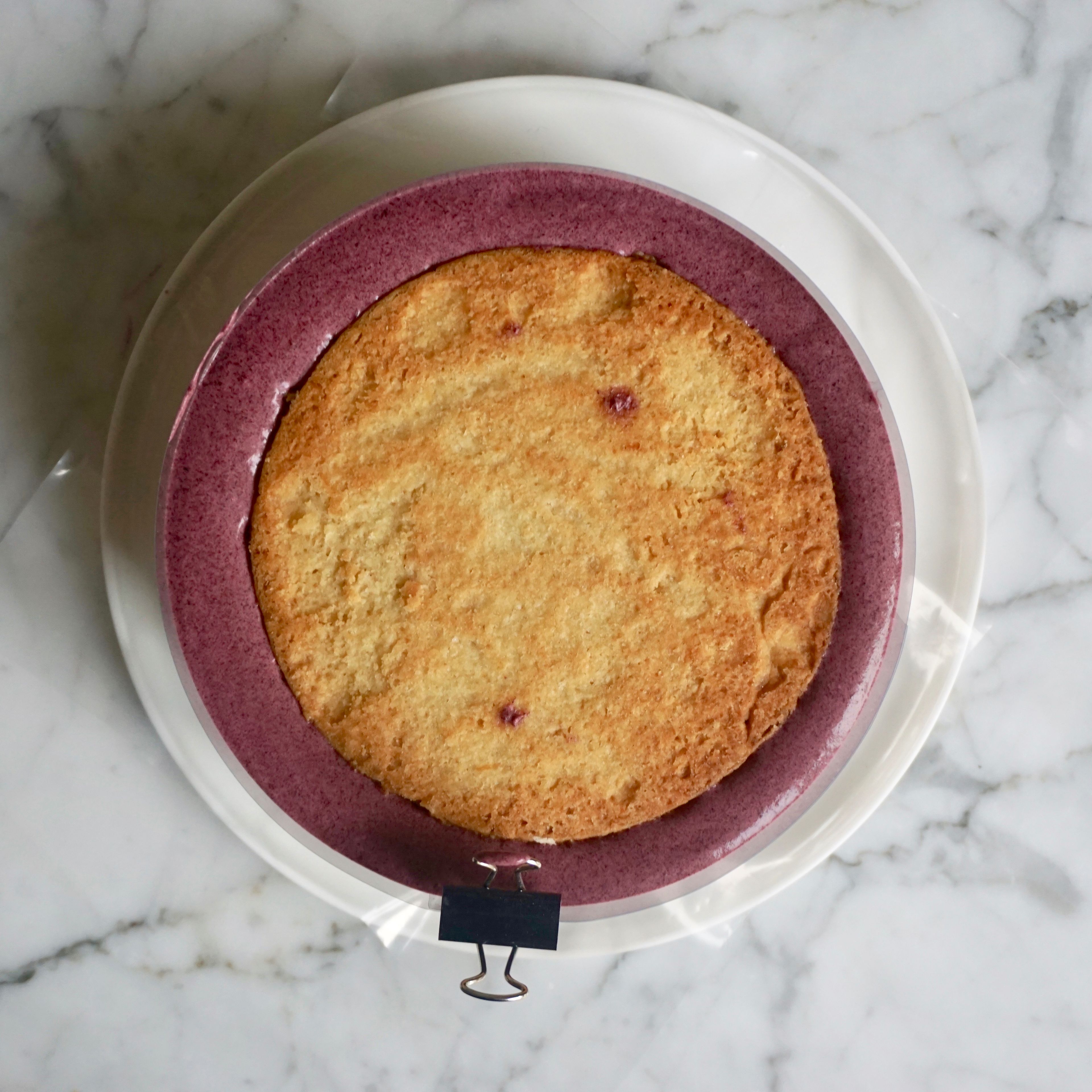 Den Kern aus Mandelbiskuit, Heidelbeerkompott und Knusperschicht leicht hineindrücken. Das Entremet für min. 6 Stunden, bestenfalls über Nacht, gefrieren. Gelatine in kaltem Wasser einweichen. Blaubeerpüree, Zucker und Glukosesirup in einem Topf aufkochen. Sahne einrühren. Alles über die weiße Schokolade gießen. Eingeweichte Gelatine zufügen und mit dem Stabmixer mixen. Glasur im Kühlschrank erkalten lassen.