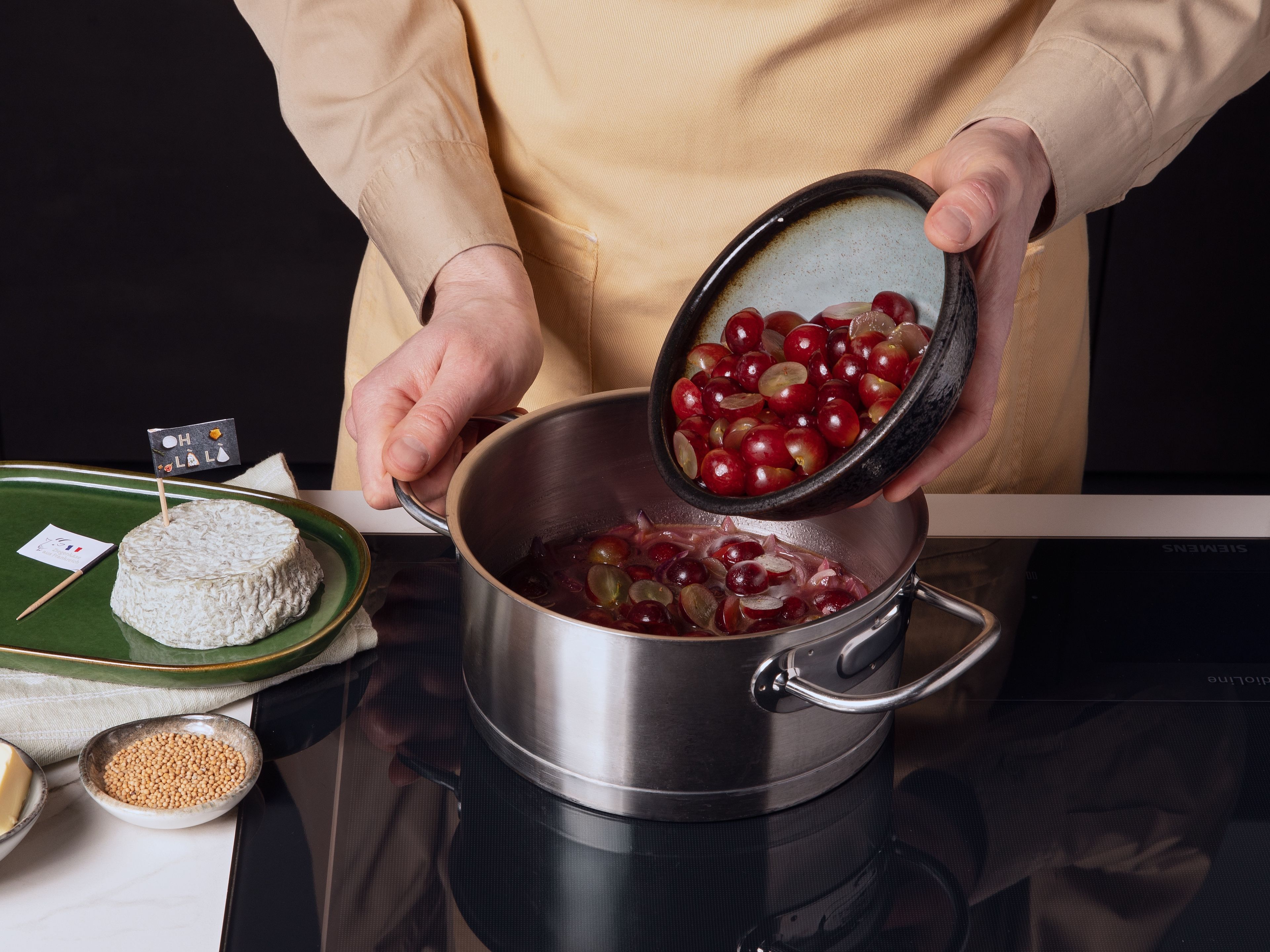 Währenddessen rote Zwiebel schälen und in feine Streifen schneiden. Die Hälfte der Weintrauben halbieren, den Rest ganz lassen. In einem mittleren Topf etwas Öl erhitzen und die Zwiebeln darin glasig andünsten. Zwiebeln mit Mehl bestäuben und umrühren. Mit Traubensaft ablöschen. Dann Weintrauben, Senfsaat und Butter zugeben und alles für ca. 8–10 Min. köcheln lassen, bis die Soße eingedickt ist.