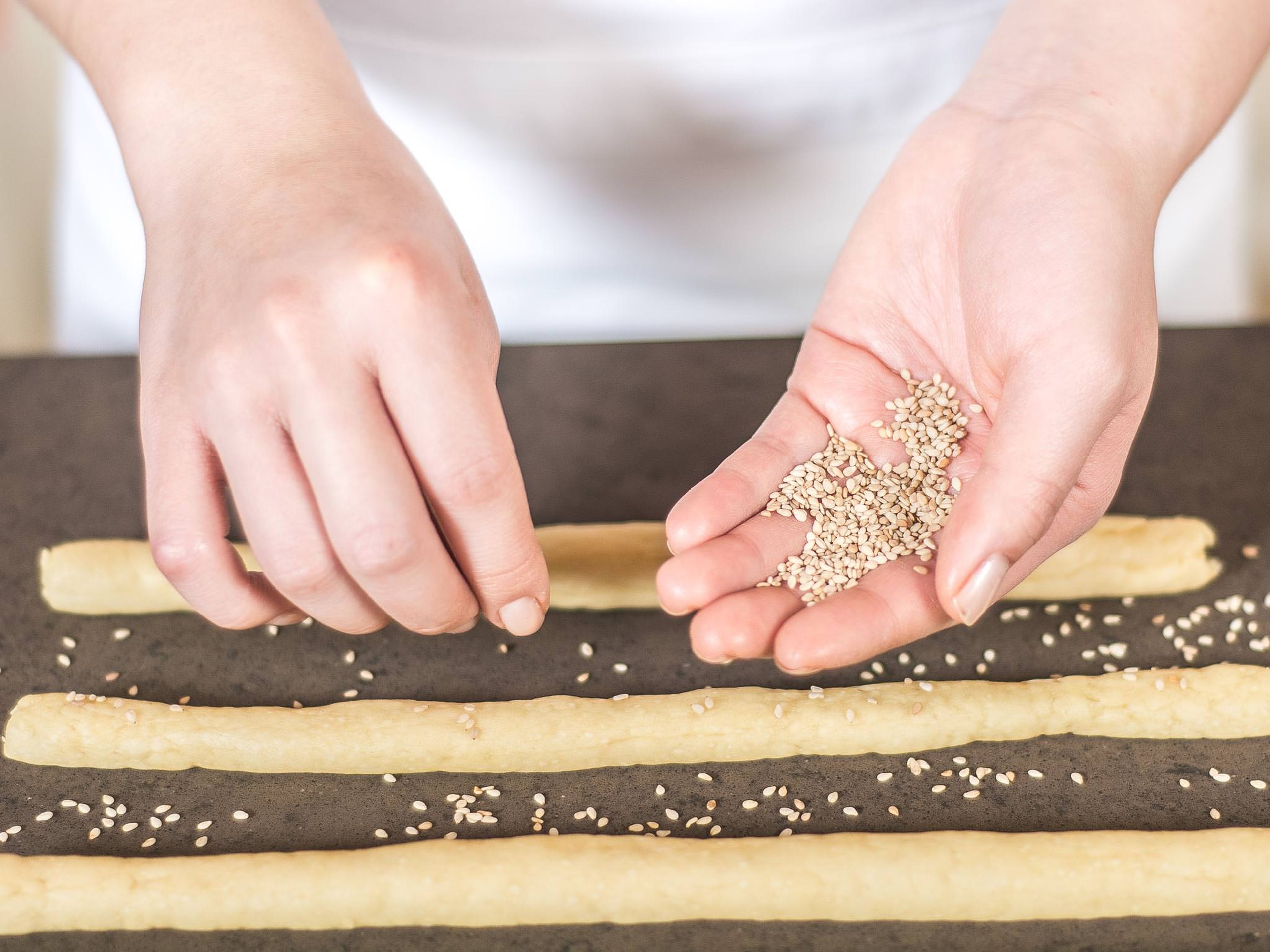 Sprinkle grissini with sesame seeds. Ideally, roll the grissini in the sesame seeds so they stick better. Place the sticks onto a lined baking tray, cover, and leave to rise in a warm place for 20 min.