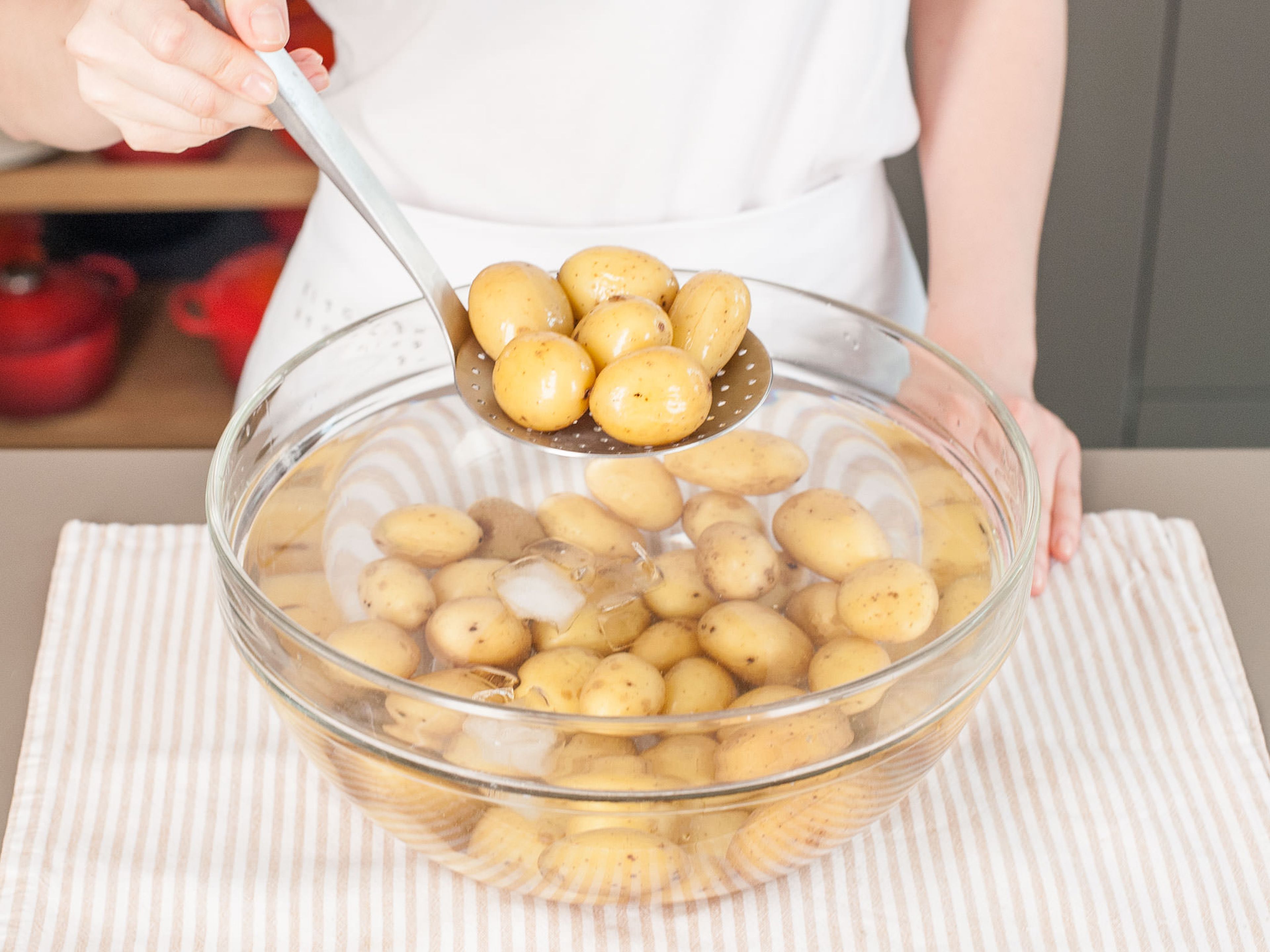 Die Kartoffeln in gesalzenem Wasser weich kochen. Danach für ein paar Minuten im Eisbad ruhen lassen und anschließend abgießen. Die Kartoffeln halbieren oder abhängig von der Größe vierteln. In eine große Rührschüssel geben.