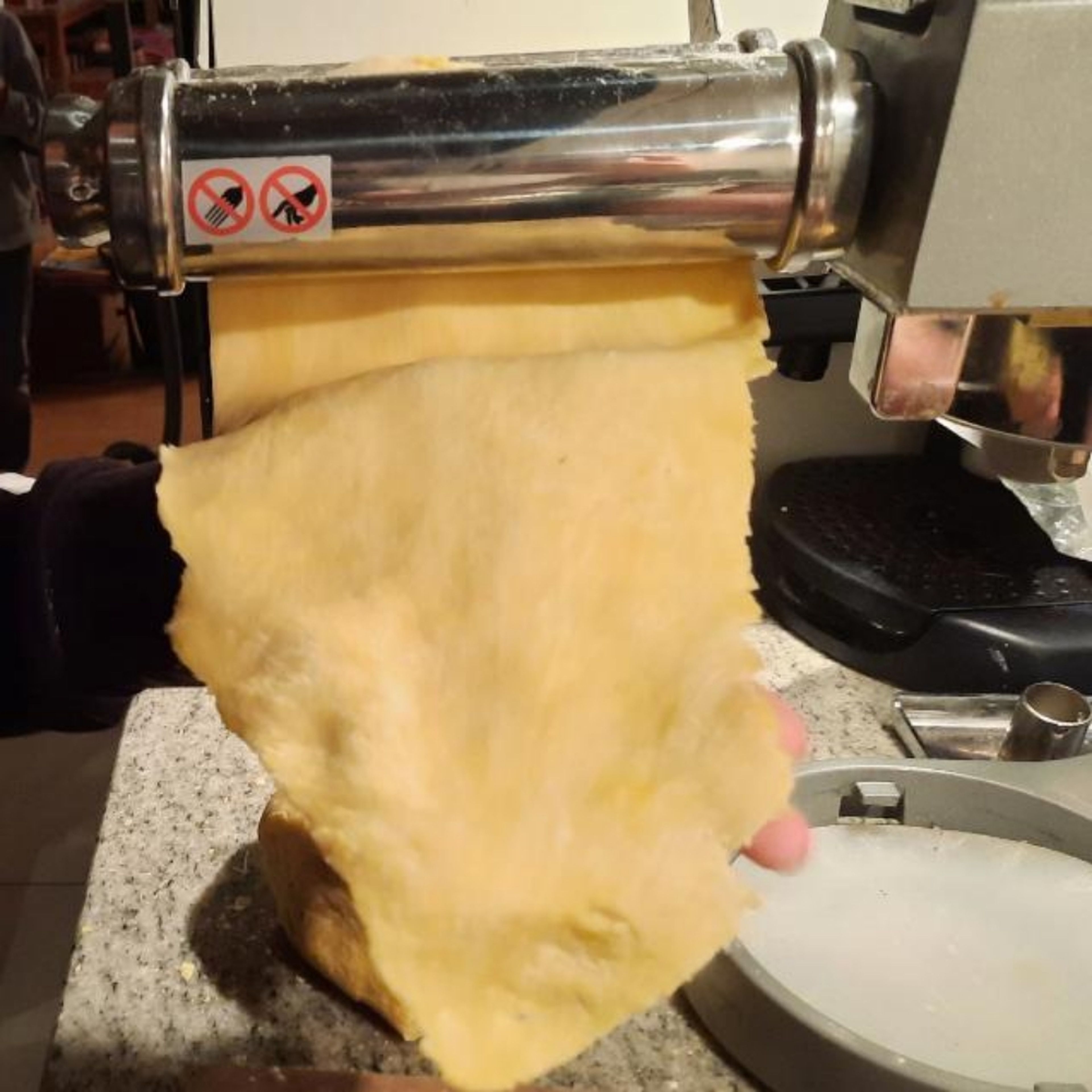 Jetzt musst du den Teig in acht Stücke teilen und zu einem flachen Rechteck formen. Wenn du mit einer Nudelmaschine arbeitest, musst du den portionierten Nudelteig öfters durch sie walzen. Hierbei solltest du etwas dicker anfangen und bei jedem Mal etwas dünner werden. Falls du keine Nudelmaschine hast, walzt du den Teig einfach so dünn wie möglich.