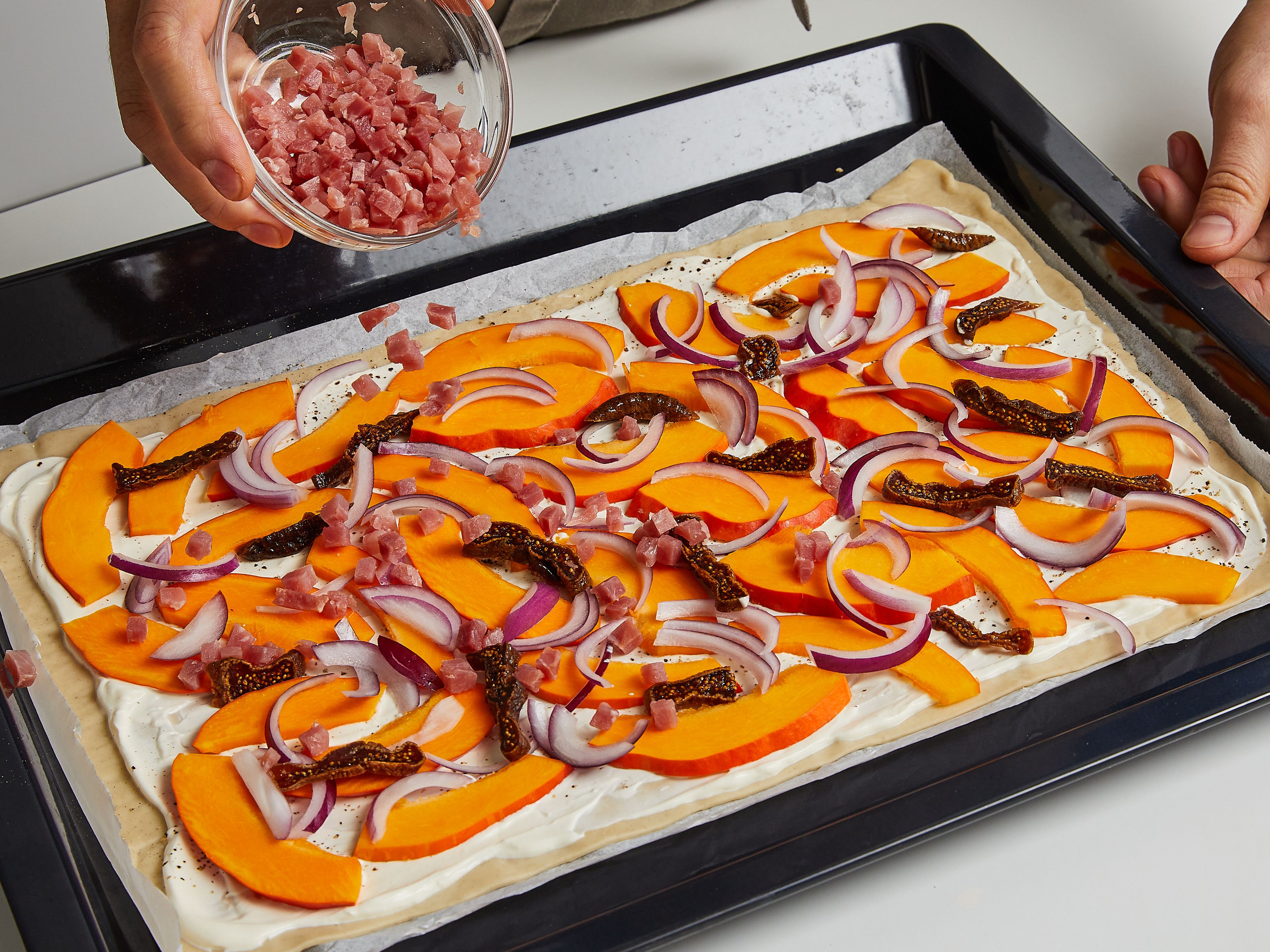 Spread the tarte flambée dough on a baking sheet lined with baking paper, spread with sour cream, leaving approx. 1 cm/ 0.4 in. border at the edge. Sprinkle sour cream with a little salt and pepper. Top tarte flambée with pumpkin strips, fig slices, onion strips and diced bacon.