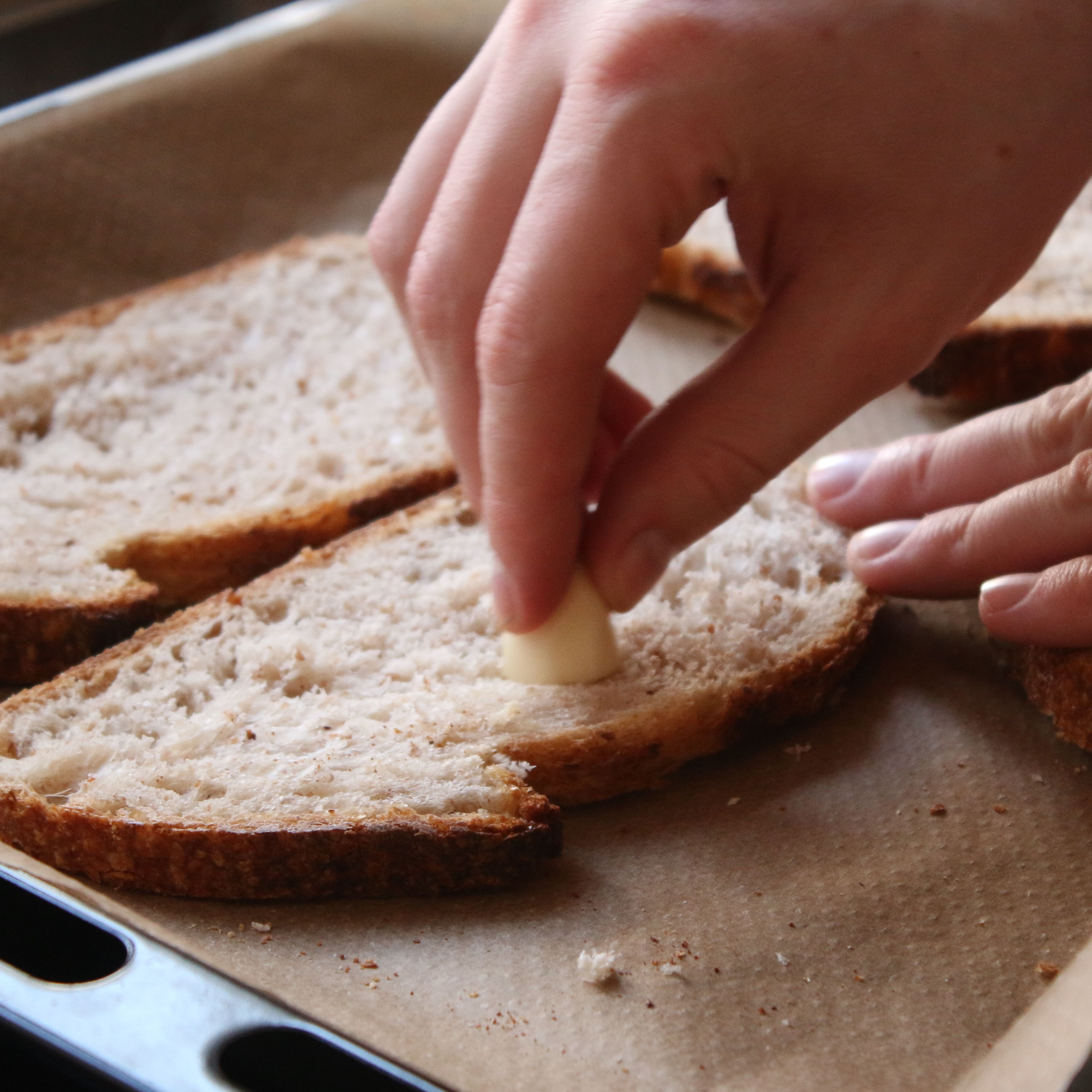 Die Knoblauchzehe halbieren und mit der Schnittseite die Brotscheiben bestreichen. Die Brotscheiben anschließend im Backofen leicht anrösten.