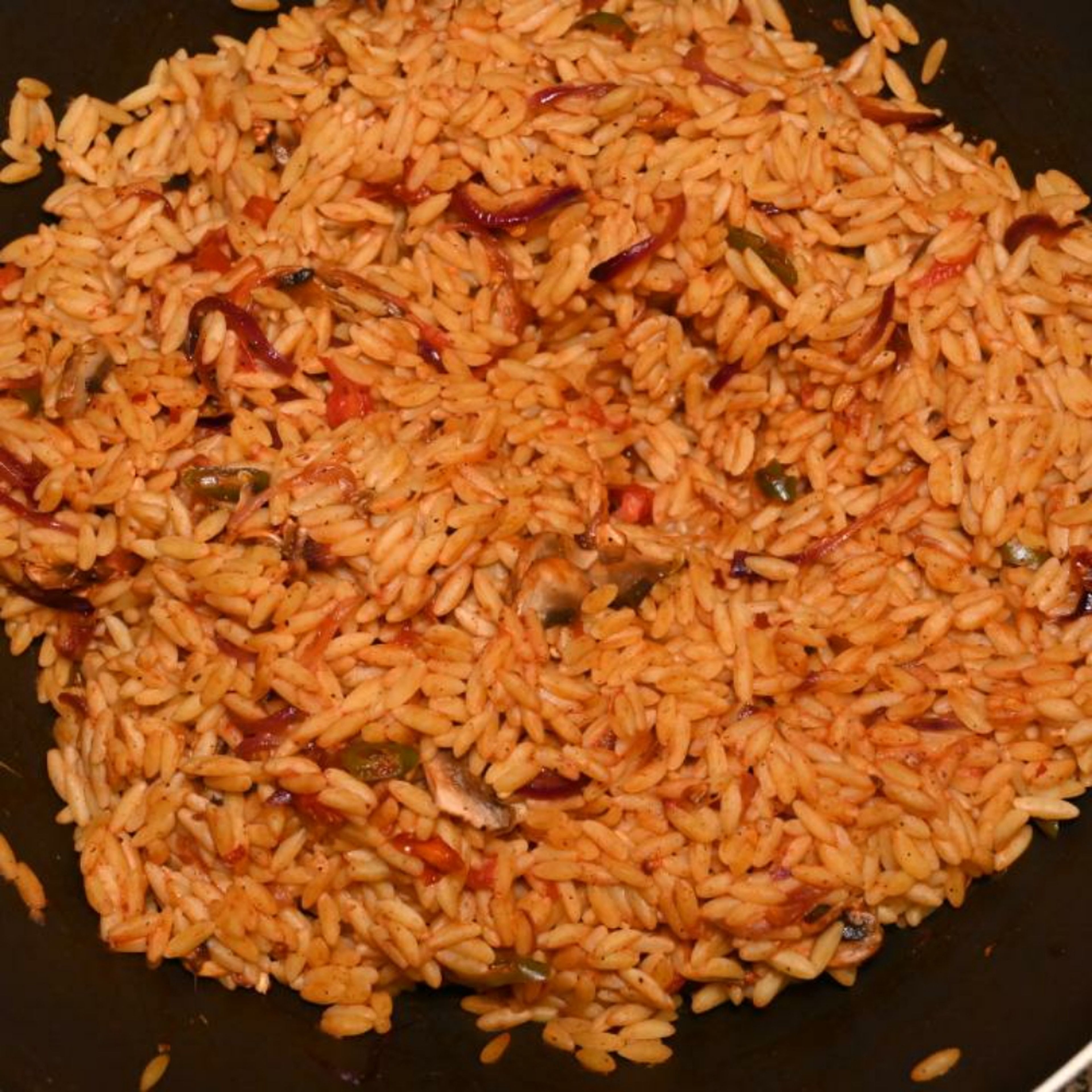 Add the cooked Orzo pasta to the wok containing all the spices, mushrooms, tomatoes, and mix to combine all the ingredients.