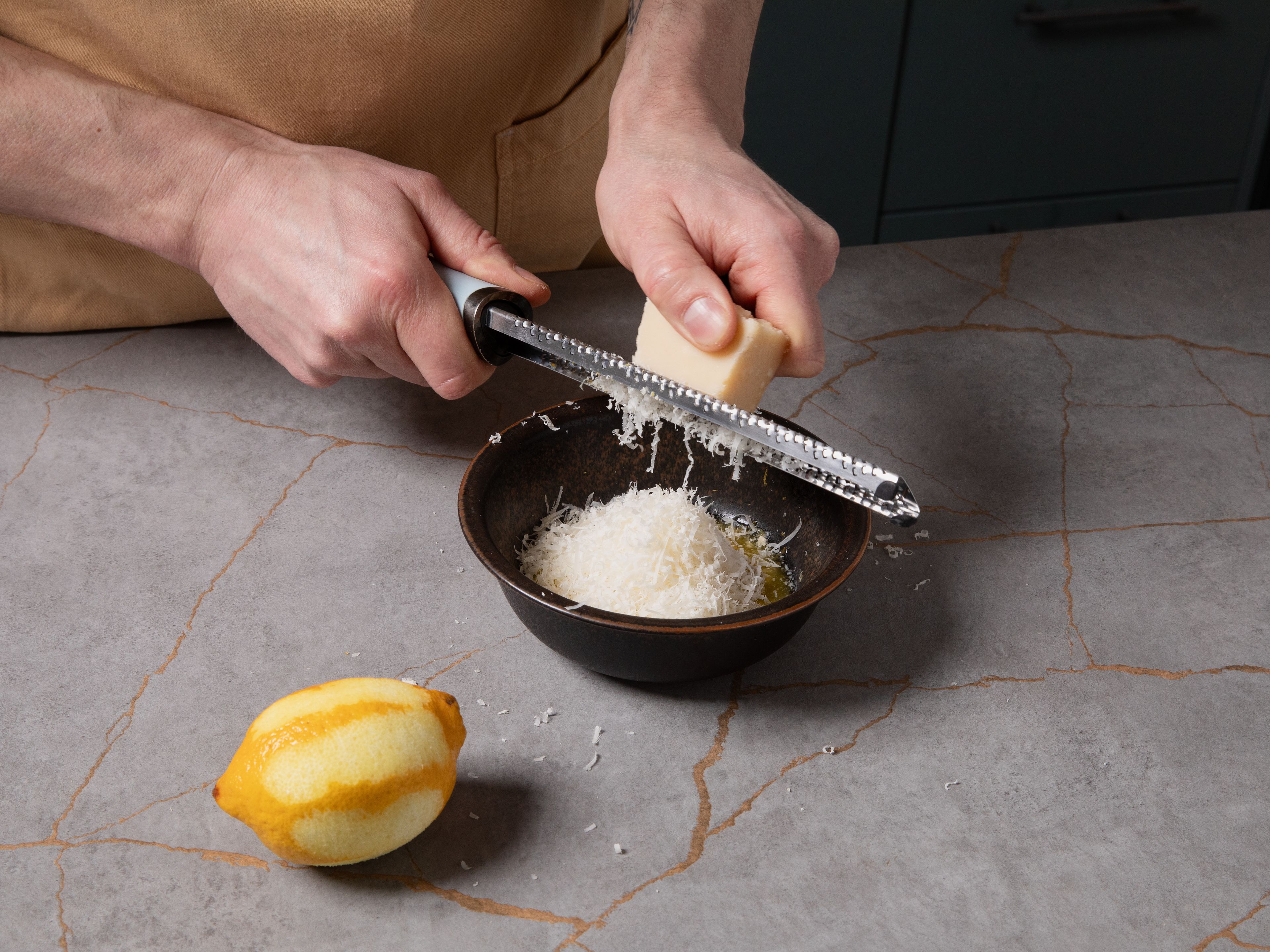 In the meantime, melt butter in a pot and finely grate the Parmesan. Zest the lemon, then slice it into thin rounds. Peel and finely chop the garlic cloves. Combine the melted butter, garlic, lemon zest, and half of the Parmesan in a bowl.
