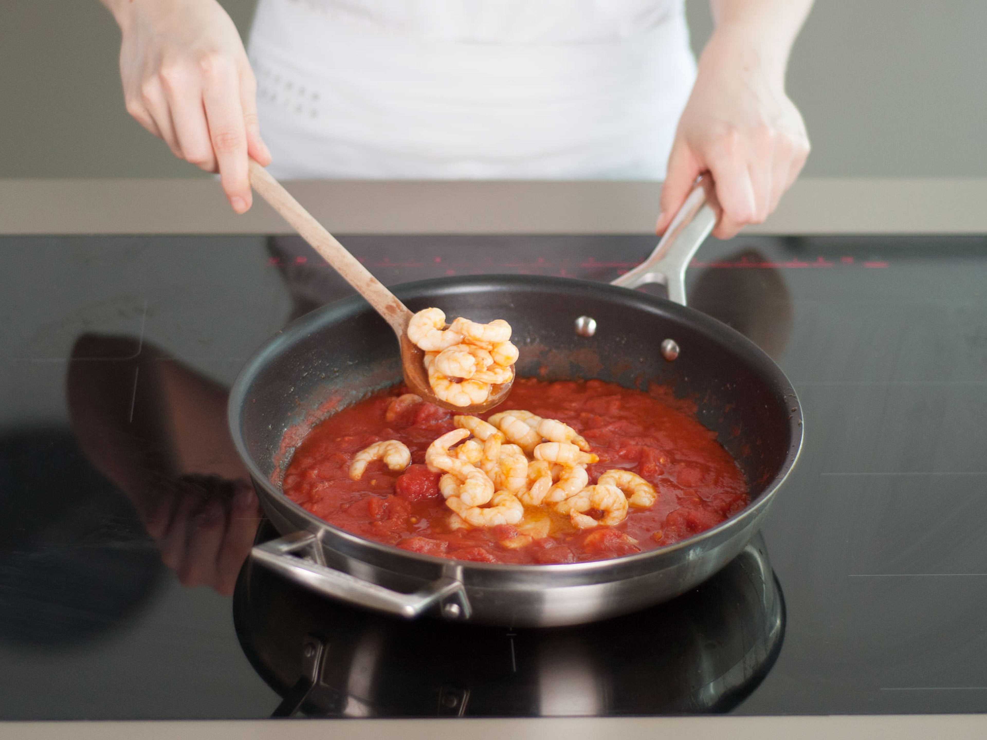 Garnelen zusammen mit ihrem Saft in eine Schüssel geben, dannn stückige Tomaten mit Knoblauch und etwas Salz in die Pfanne geben. Bei mittlerer Hitze aufkochen. Dann Hitze verringern, Garnelen dazugeben und abdecken, während die Polenta zubereitet wird.