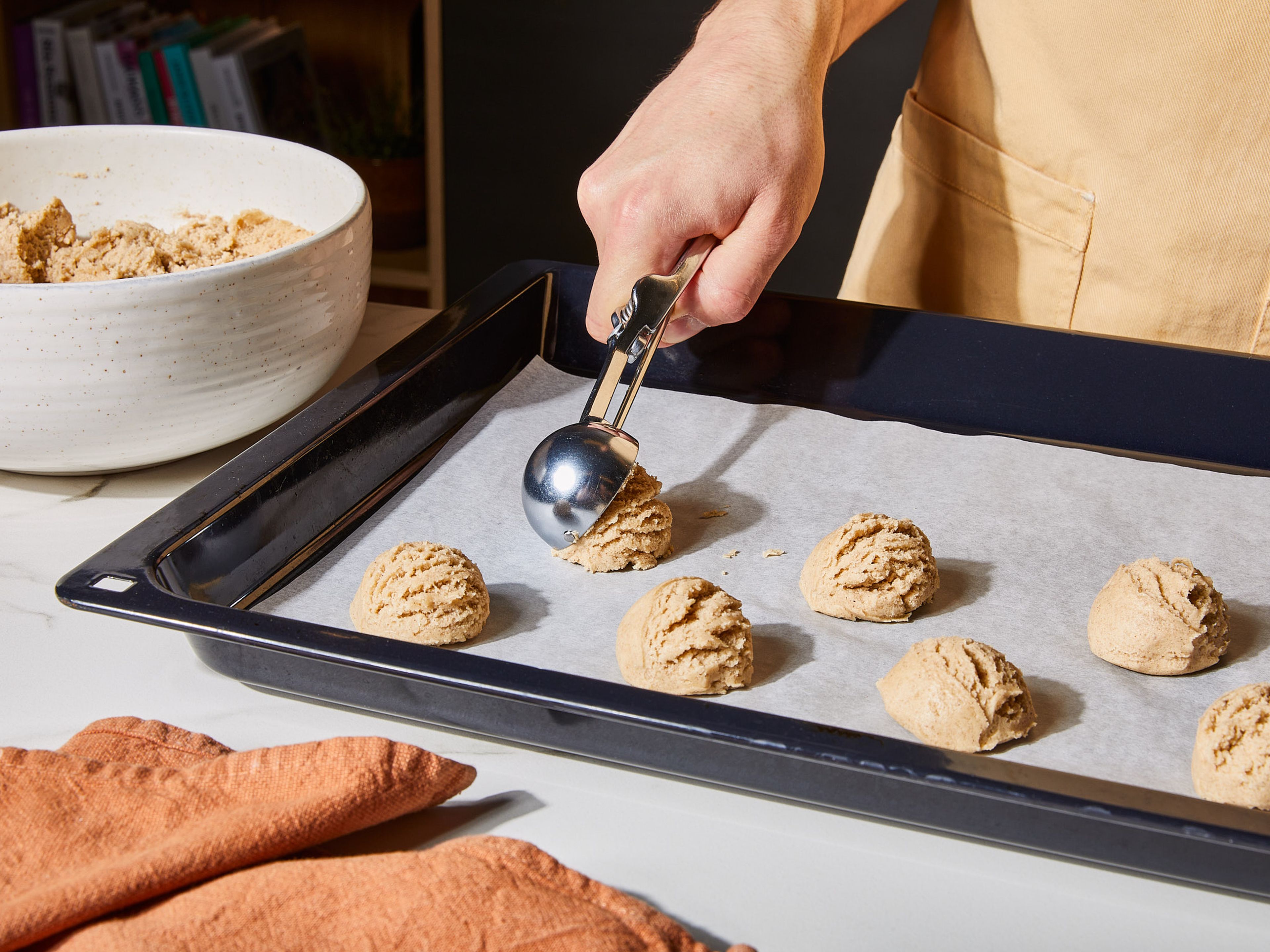 Mit einem Eisportionierer oder einem großen Löffel jeweils einen Cookie formen und auf ein mit Backpapier ausgelegtes Backblech legen. Etwas Platz zwischen den Keksen lassen, da sie beim Backen auseinanderlaufen. Das Backblech in den Ofen schieben und ca. 8–12 Min. backen, je nach Ofen: Die Ränder sollten leicht braun sein, die Mitte jedoch noch fast roh aussehen. Cookies vor dem Dekorieren vollständig auskühlen lassen.