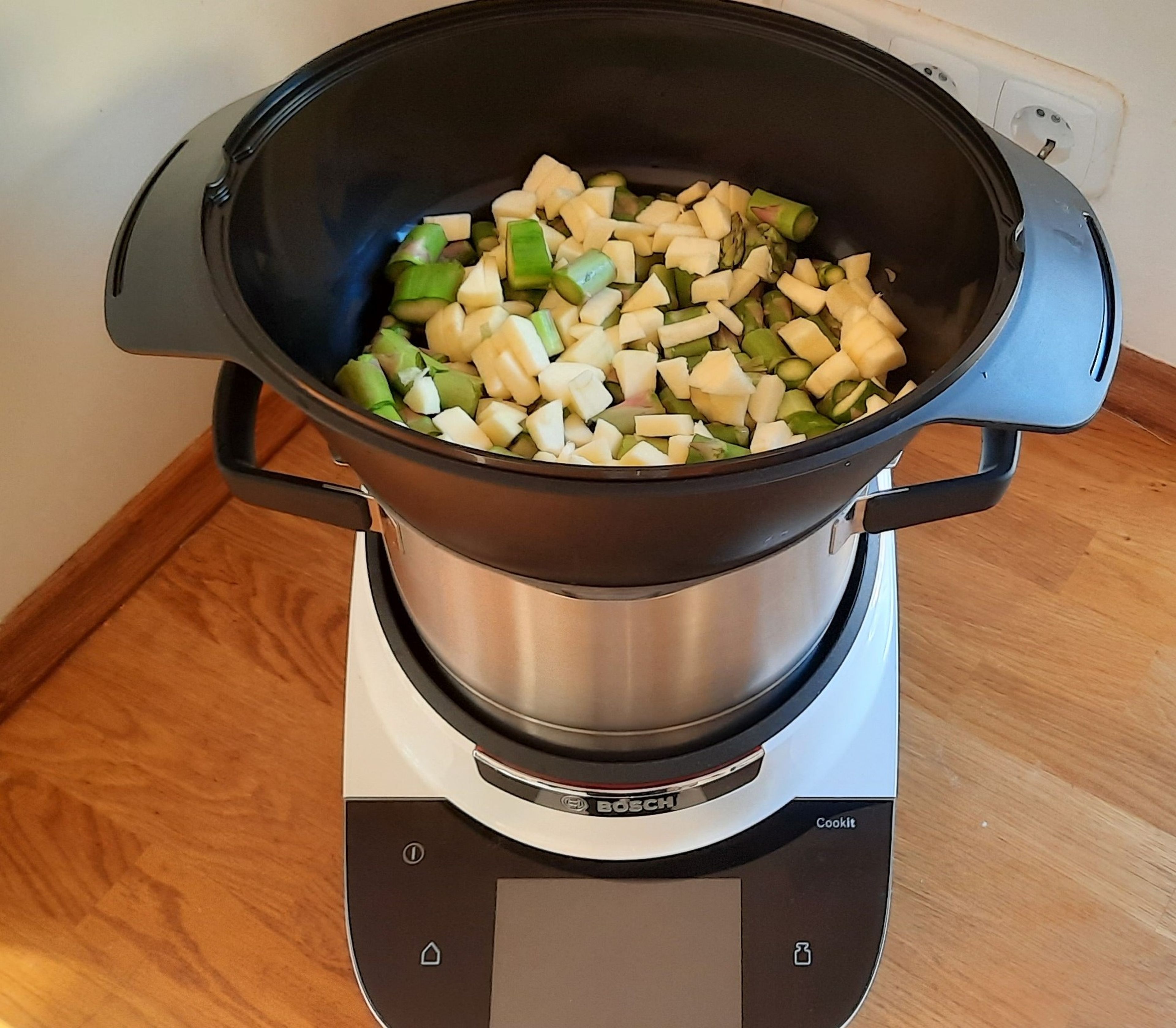 Wenn nötig die Enden des grünen Spargels schälen und den Spargel dann in ca. 2 cm große Stücke schneiden. Die beiden Äpfel schälen und würfeln. In den Cookit das Wasser geben und den Dampfgaraufsatz daraufstellen. Den Spargel und die Äpfel hineingeben und ohne Deckel alles im Automatikprogramm dampfgaren (Dampfgaraufsatz I Hohe Intensität I 10 Min.).
