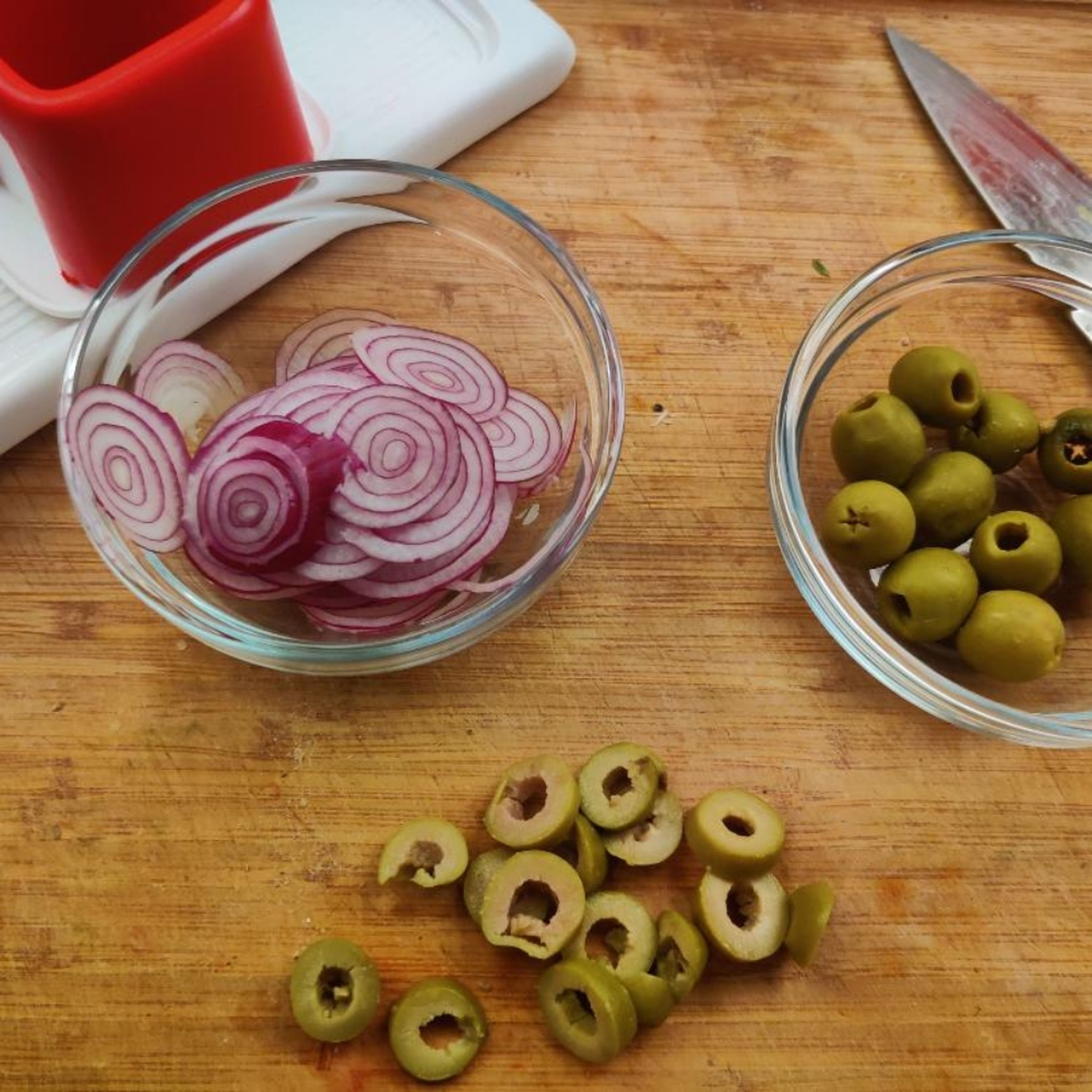 Backofen auf 200°C (Umluft, 220g Ober-Unterhitze) vorheizen. Die Oliven in Ringe schneiden. Die Zwiebel dünn hobeln (oder mit einem Messer in dünne Scheiben schneiden). Die Zwiebelscheiben auseinander nehmen, so dass Ringe entstehen.