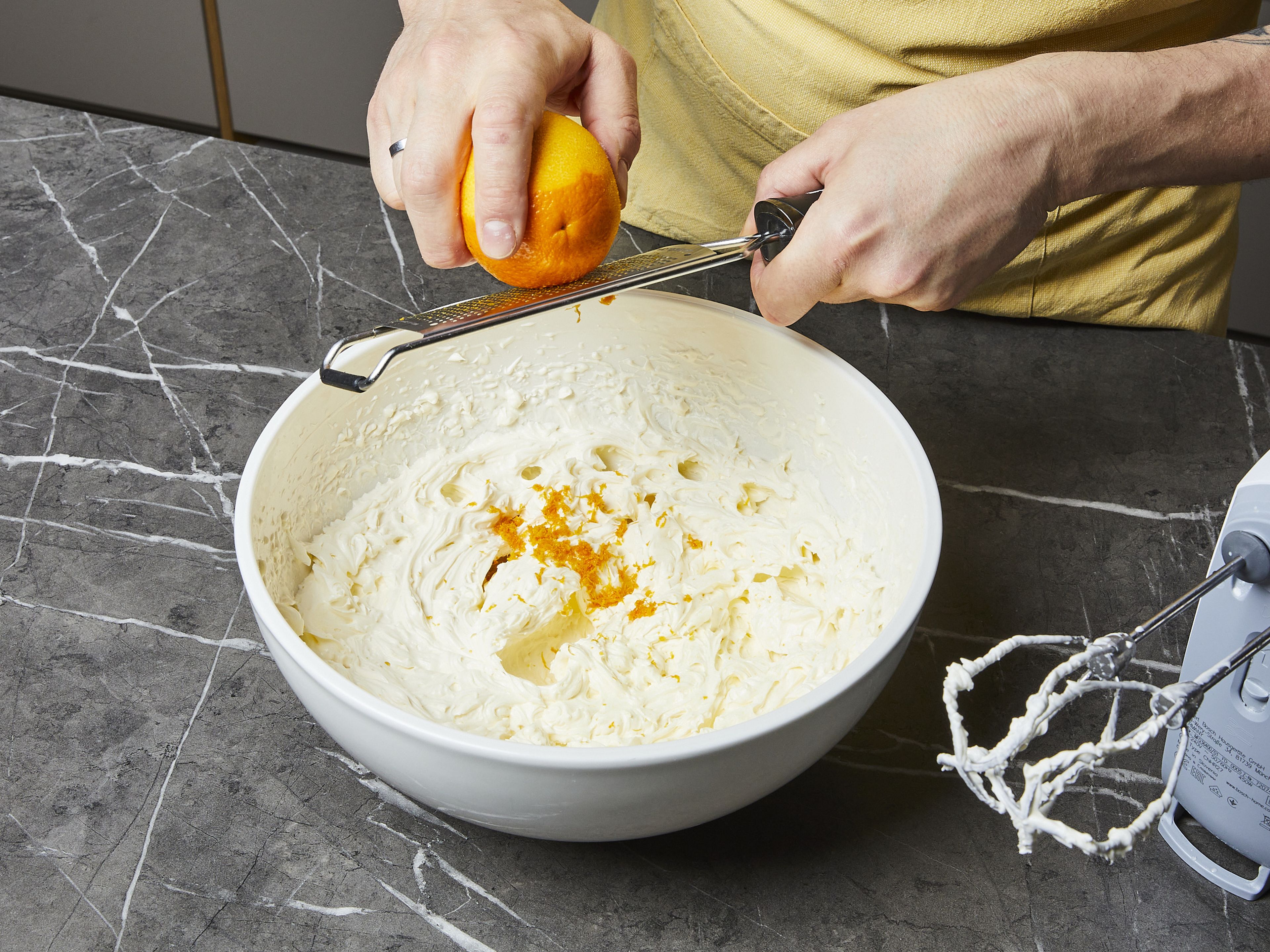 Für die Mascarpone-Creme die Schale einer Orange fein abreiben. In einer großen Schüssel Mascarpone, Orangenabrieb, restlichen Zucker und Schlagsahne vermischen und mit einem Handrührgerät steif und schaumig schlagen.