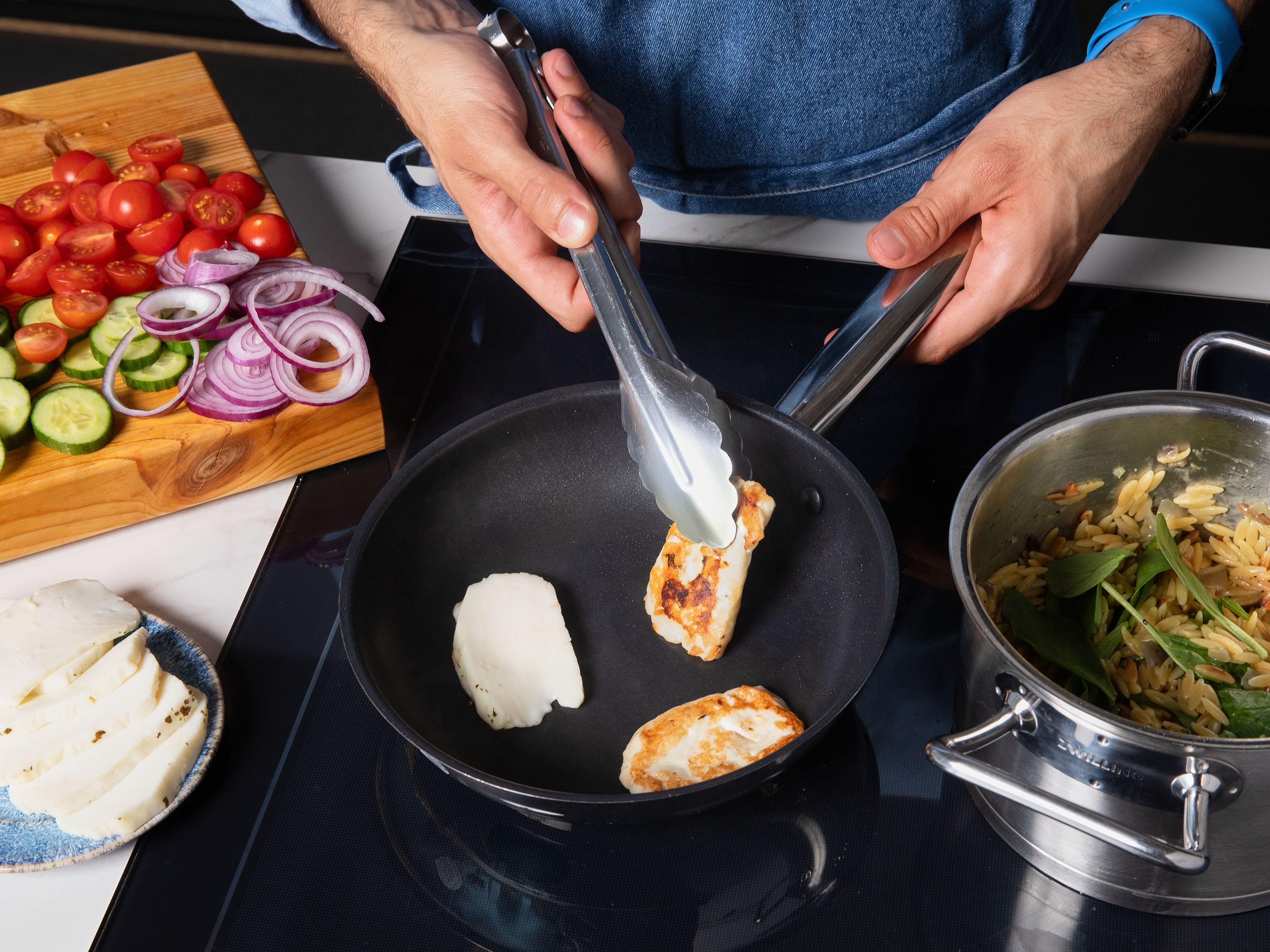 Cut halloumi into approx. 1 cm/0.4 in. thin slices and fry in a pan until both sides are golden brown for approx. 6 min. in total. Check on the orzo and mix in spinach leaves and lemon zest approx. 2 min. before it is done. Then, remove from heat and let cool a bit.
