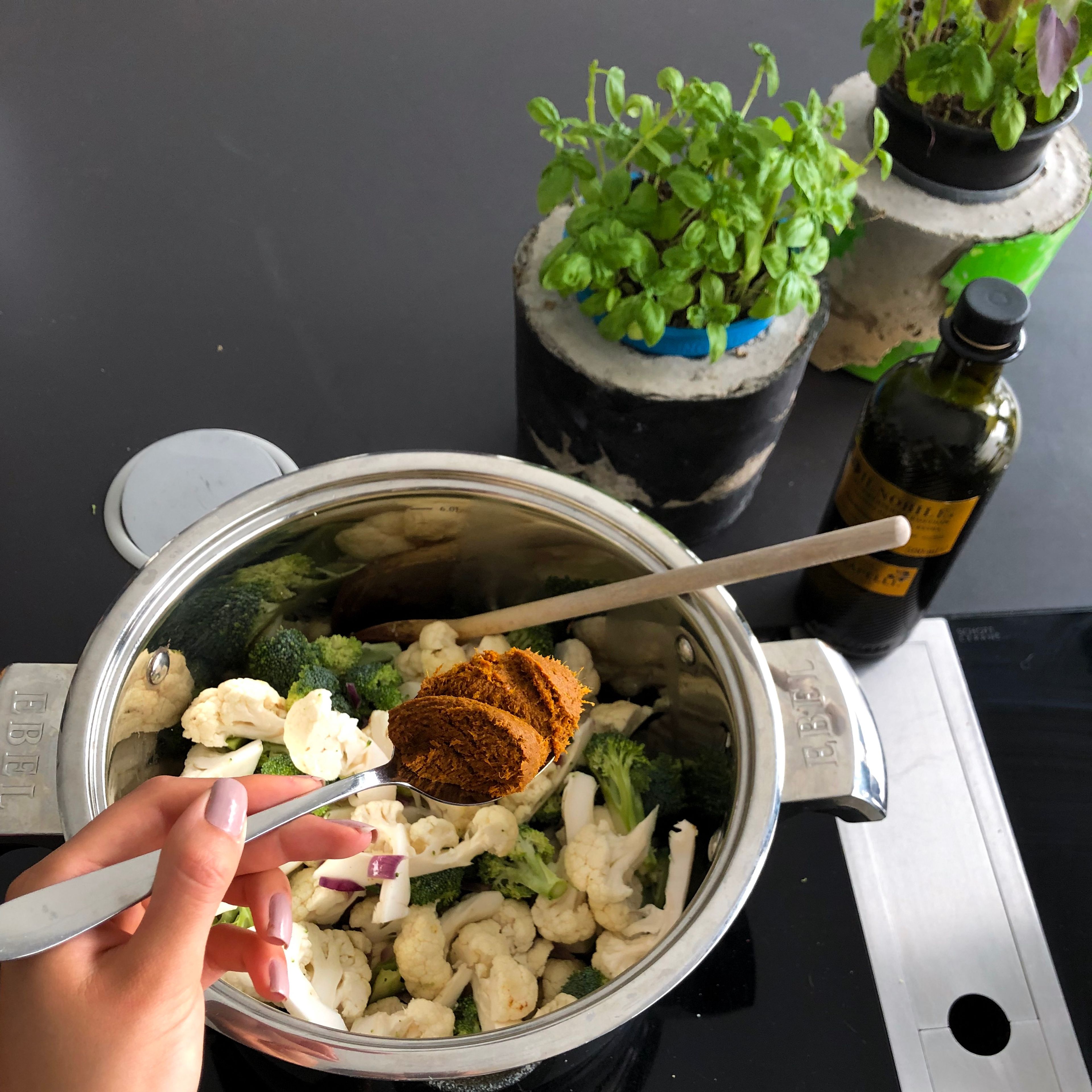 Blumenkohl, Brokkoli und Currypaste zu den Zwiebeln hinzufügen und drei Minuten mitdünsten. Je nach gewünschter Schärfe kann man zwischen roter und gelber Currypaste wählen.