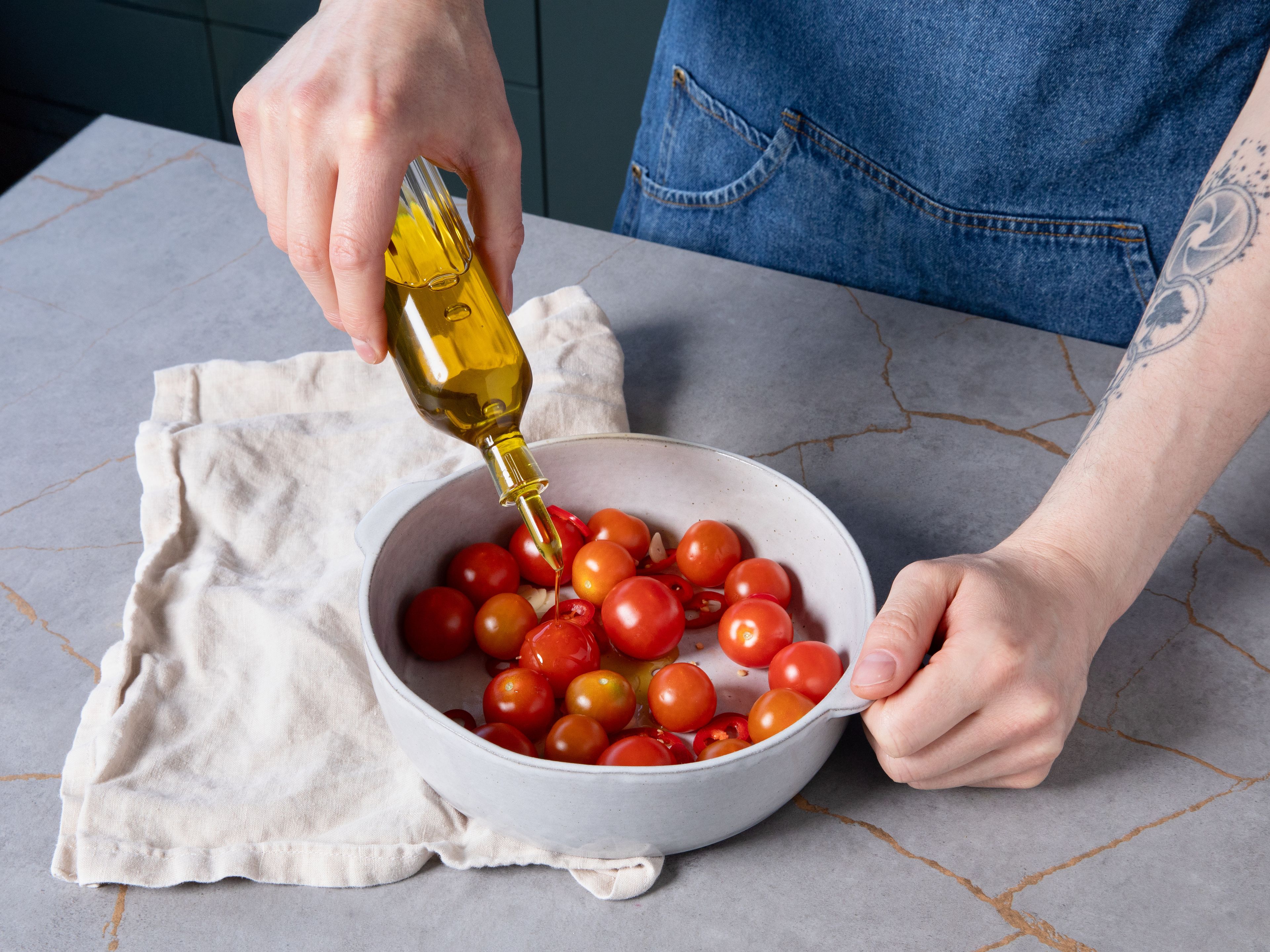 Den Ofen auf 150 °C Umluft vorheizen. Knoblauch schälen und fein schneiden. Chili in feine Ringe schneiden. Tomaten zusammen mit der Hälfte des Knoblauchs und der gesamten Chili in eine ofenfeste Form geben. Mit Olivenöl beträufeln, leicht salzen und im Ofen ca. 20–30 Min. confieren, bis die Tomaten weich sind und leicht aufplatzen.