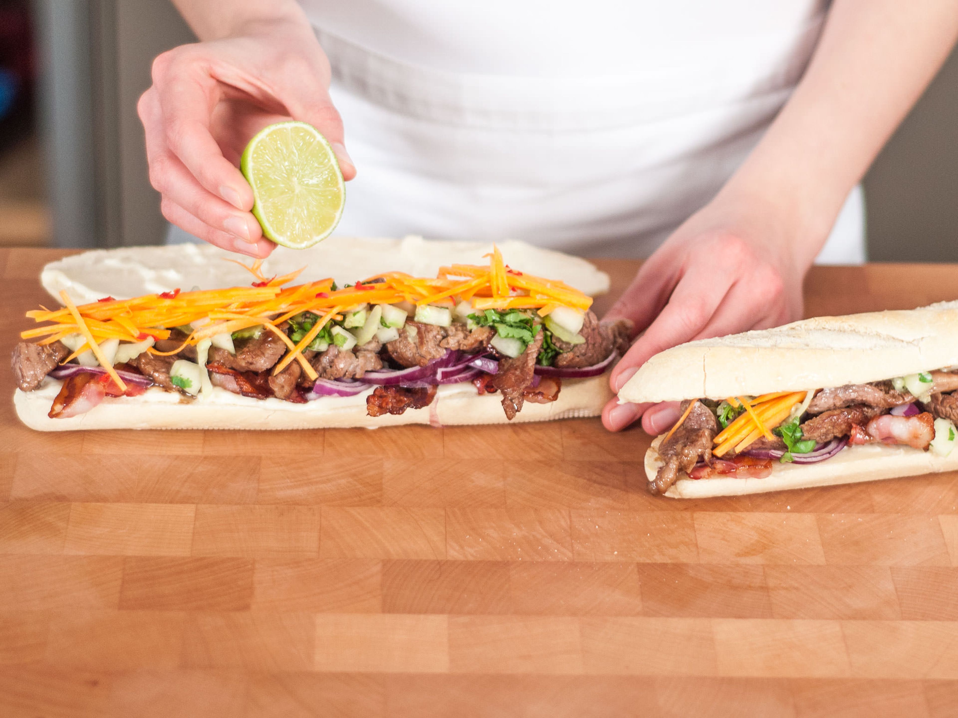 Cut baguette lengthwise, but not all the way through. Spread top and bottom layer of baguette with mayonnaise. Layer with bacon, beef, vegetables, and herbs. Garnish with remainder of chopped cilantro and top it off with a drizzle of lime juice. Enjoy!