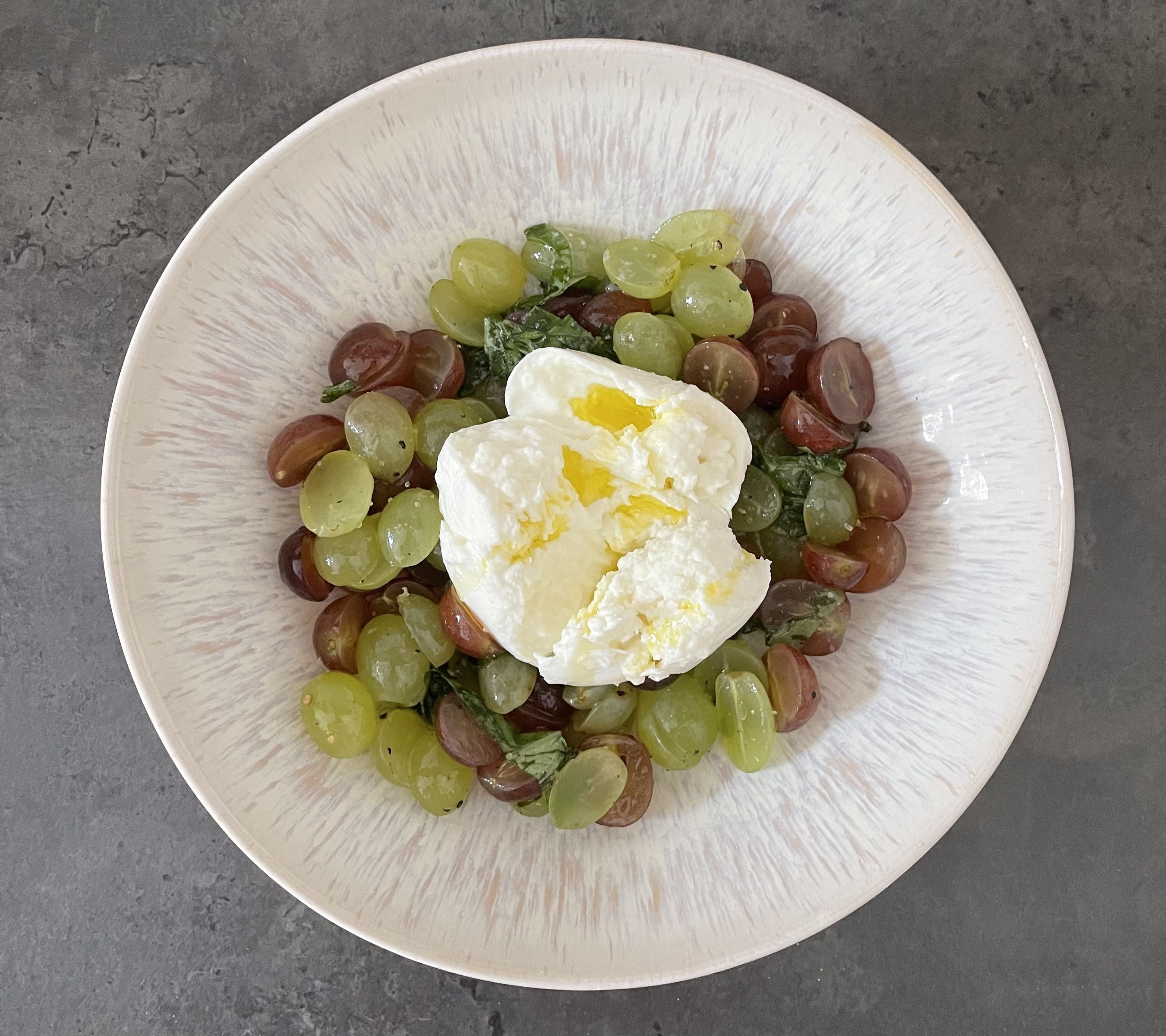Den Weintrauben-Salat auf zwei Teller verteilen und je einen Büffelmozzarella leicht zerrupfen und darauf platzieren. Anschließend nach Belieben mit Basilikum, Olivenöl, Salz und Pfeffer garnieren.