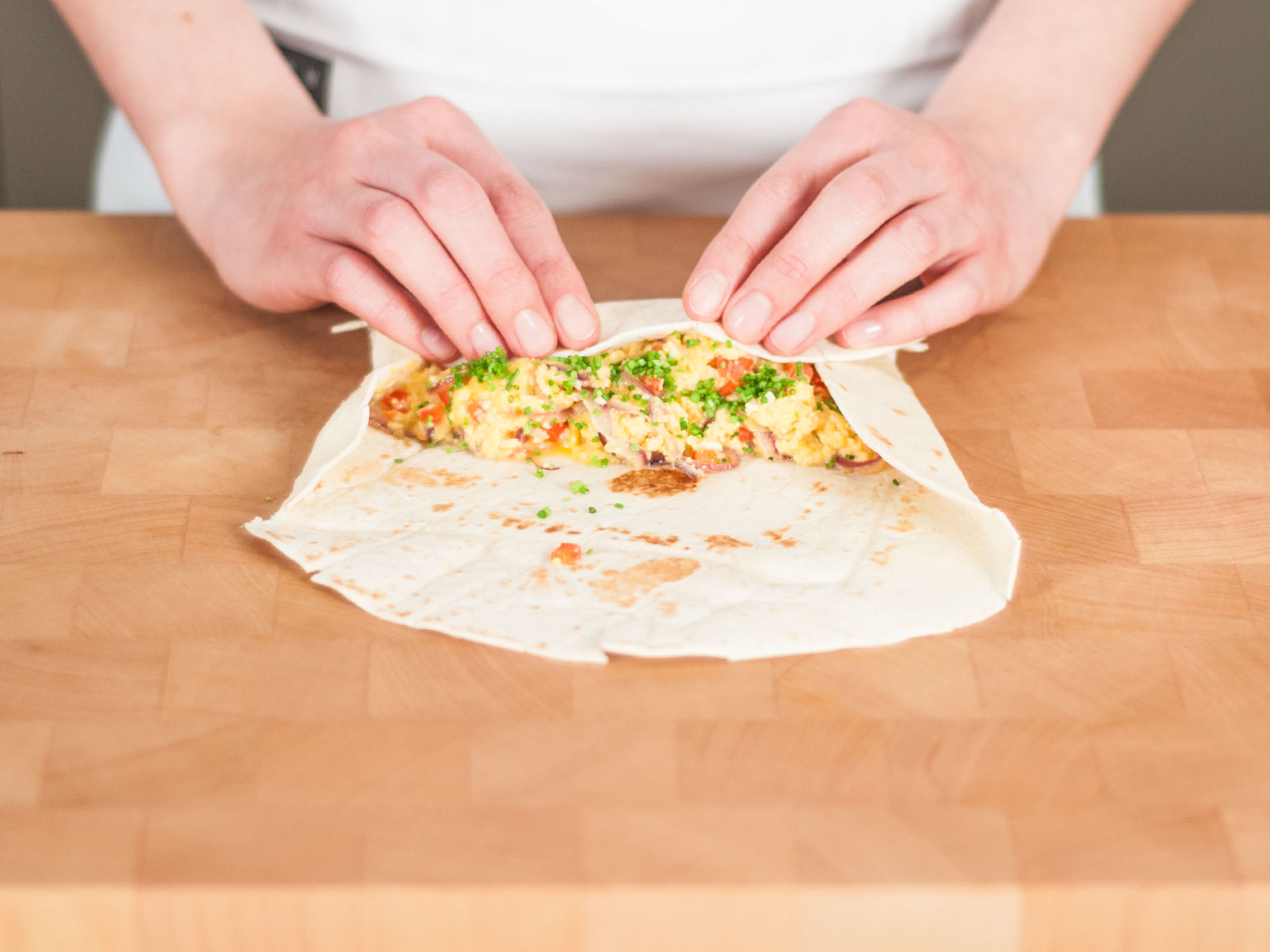 Place some of the eggs in the middle of the tortilla, taking care not to overfill. Sprinkle some chives on top. Fold tortilla in from the sides. Then, roll forward from bottom with thumbs until burrito is tightly rolled. Enjoy!
