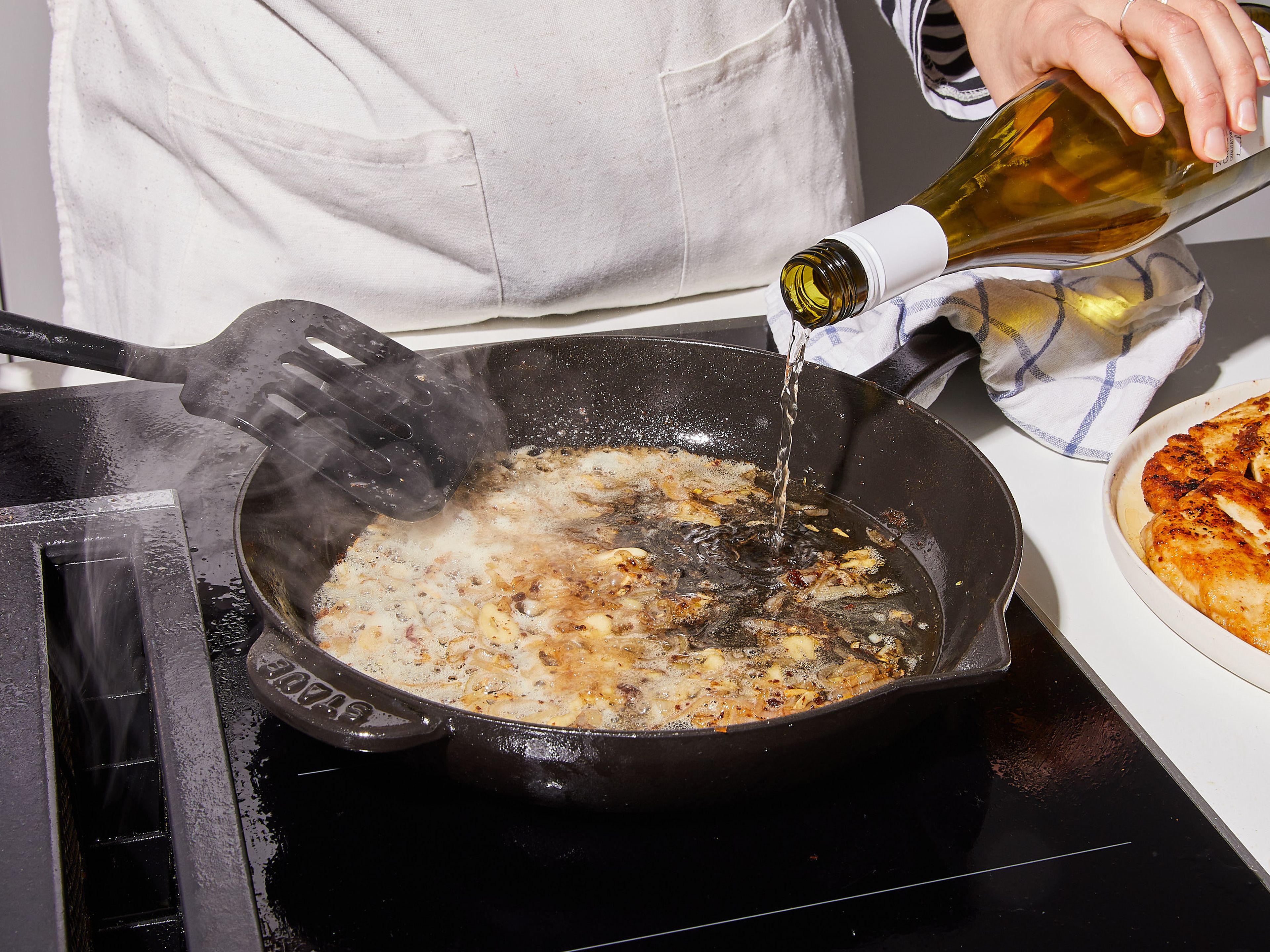 Herdplatte auf geringe bis mittlere Hitze einstellen. Bei Bedarf etwas mehr Olivenöl in die Pfanne geben. Knoblauch und Schalotte hinzufügen und unter ständigem Wenden dünsten, damit der Knoblauch nicht anbrennt. Ca. 3 Min. dünsten, bis die Schalotten glasig werden und der Knoblauch anfängt leicht zu bräunen. Wein und Kapern dazugeben und mit dem Kochlöffel die braun gebratenen Stückchen vom Boden der Pfanne lösen.
