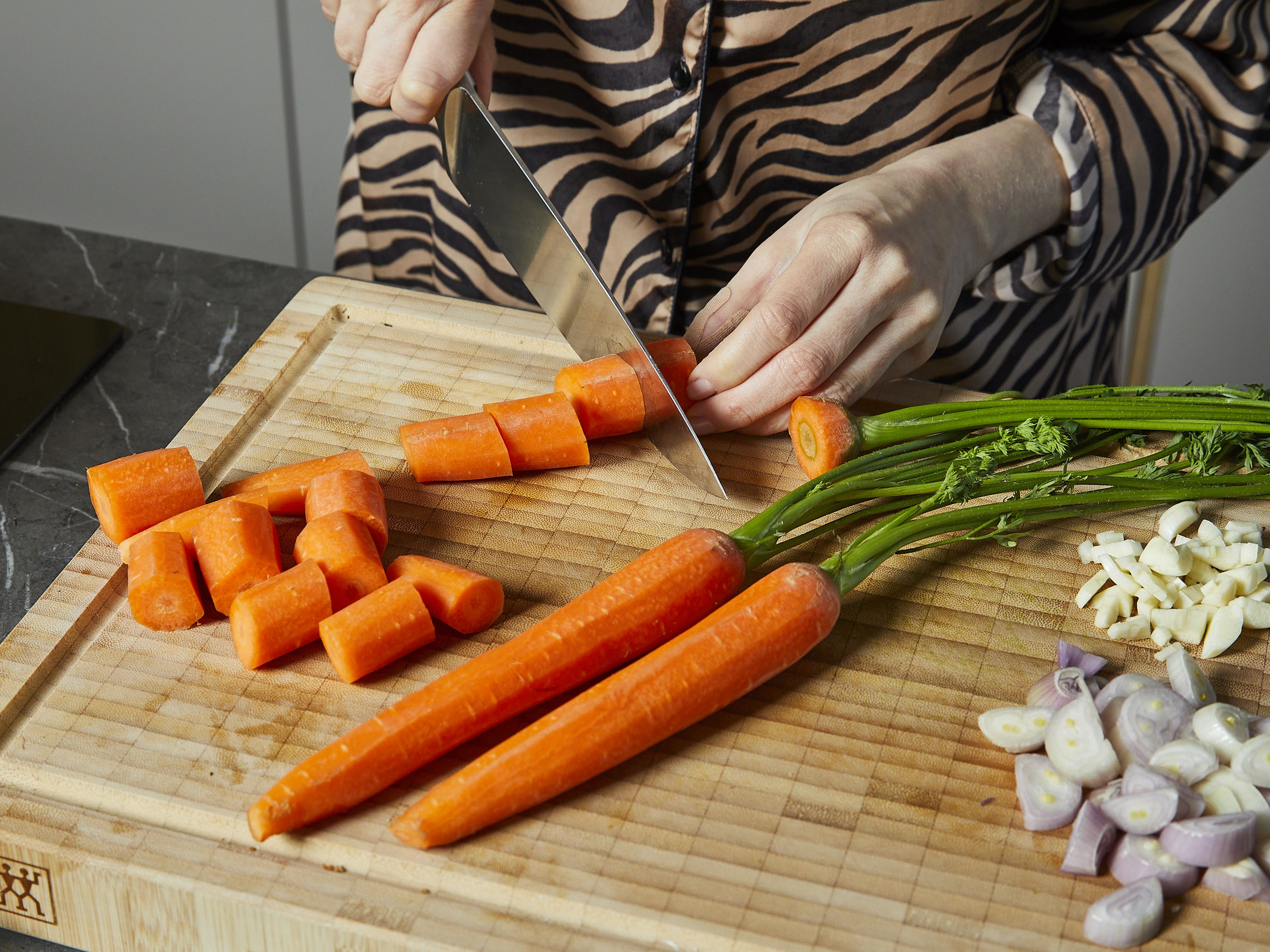 Das Karottengrün ca. 15 cm über dem Strunk abschneiden und für die weitere Verwendung beiseite legen, die Stiele und den Strunk entfernen. Den Knoblauch, die Schalotten und die Karotten schälen und grob hacken. Den Parmesankäse reiben. Die Zitrone abreiben und auspressen. In einem großen Topf das Wasser für die Nudeln zum Kochen bringen und gut salzen.