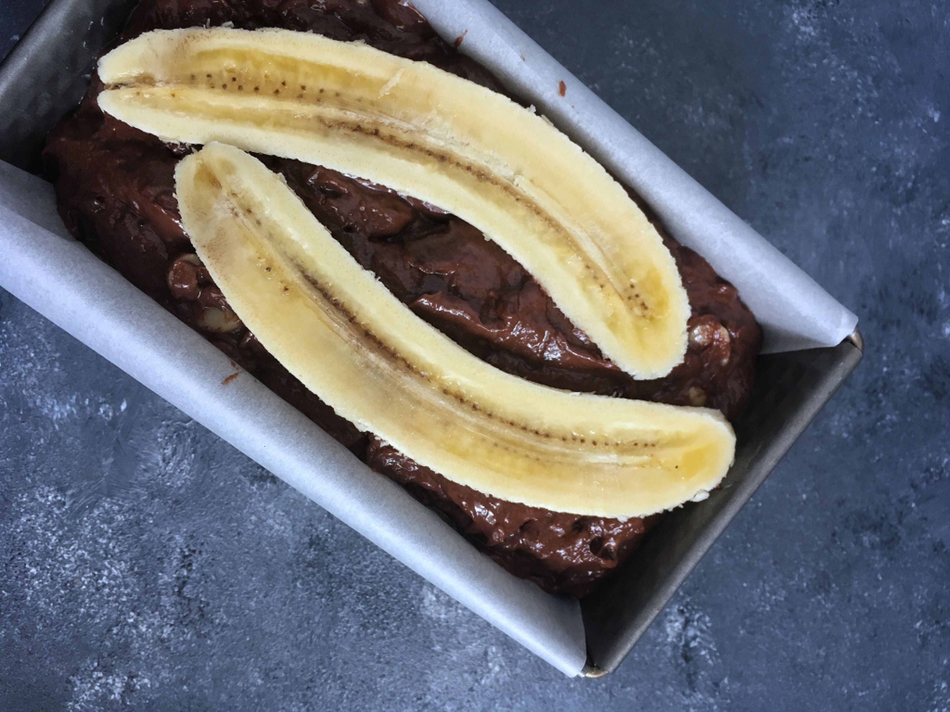 Den Schokoteig in die Form geben. Dann die übrige Banane der Länge nach halbieren und mit dem braunen Zucker bestreuen. So karamellisiert das beim Backen so schön.