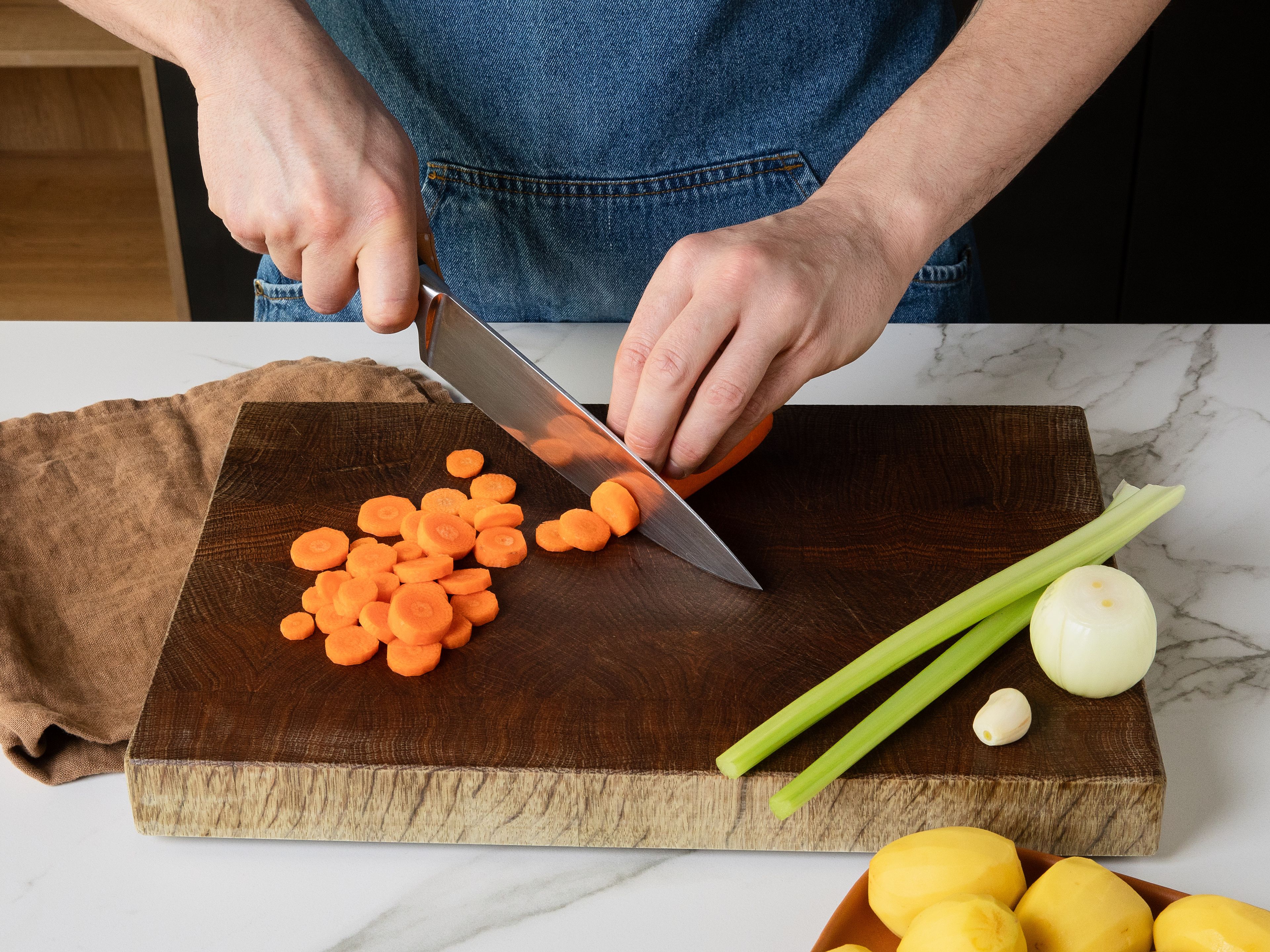 Die Kartoffeln schälen und in ca. 1 cm große Würfel schneiden. Karotten schälen und in dünne Scheiben schneiden. Den Sellerie ebenfalls in kleine Scheiben schneiden. Zwiebel schälen und fein würfeln. Die Knoblauchzehen schälen und fein hacken. Öl in einem großen Topf erhitzen, Zwiebeln, Karotten, Sellerie und Knoblauch darin ca. 5 Min. glasig anbraten.