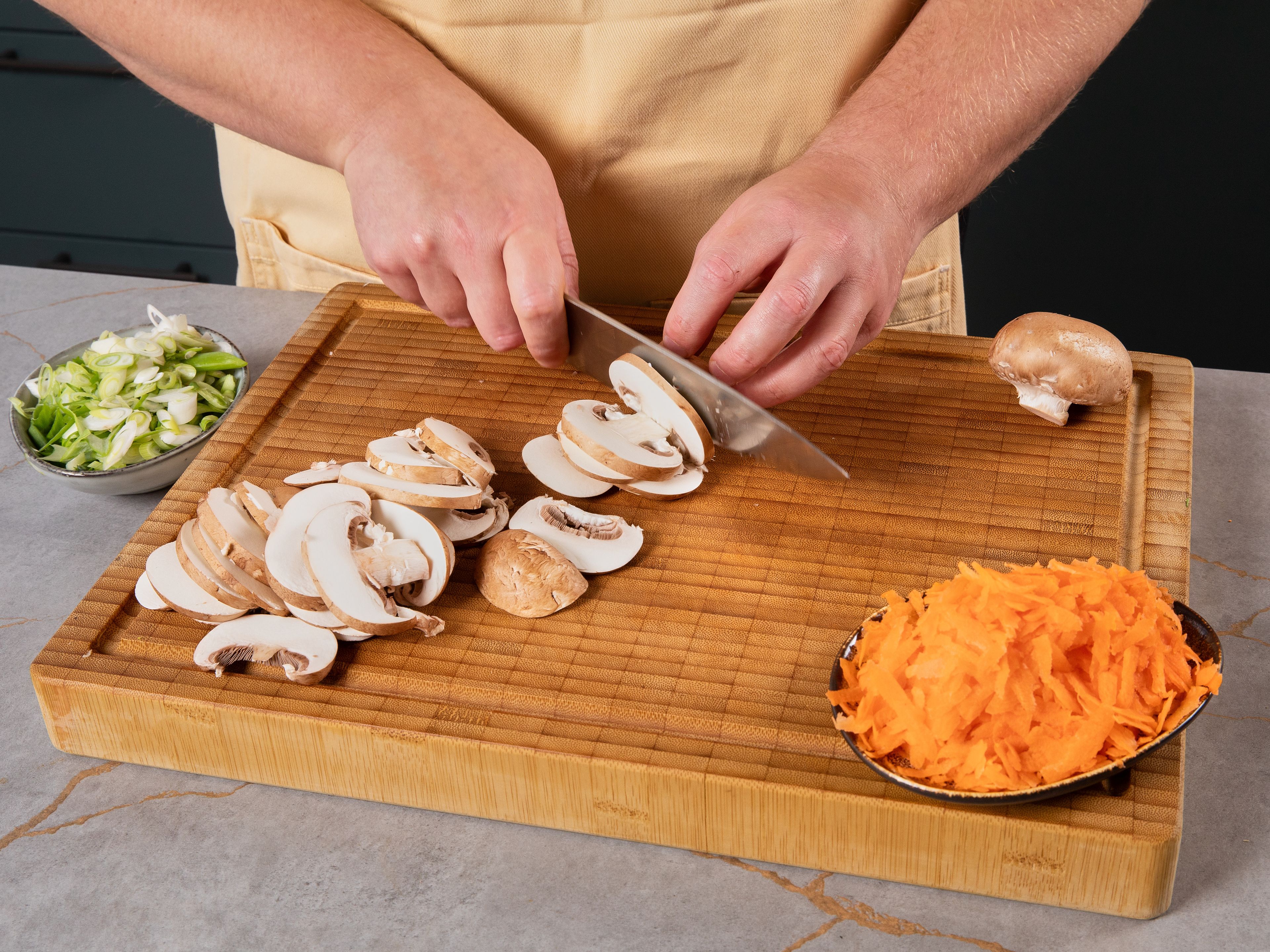Den Backofen auf 220°C vorheizen. Eine rechteckige Auflaufform einfetten. Den Klebreis nach Packungsanleitung kochen und beiseite stellen. In einer kleinen Schüssel Gochujang, Sojasauce, Sesamöl, Honig und Reisessig verquirlen und beiseite stellen. Die Champignons in Scheiben schneiden, die Zwiebel in Würfel schneiden, den Knoblauch fein hacken, den Spinat grob hacken, die Karotten schälen und raspeln, die Frühlingszwiebeln in Ringe schneiden.