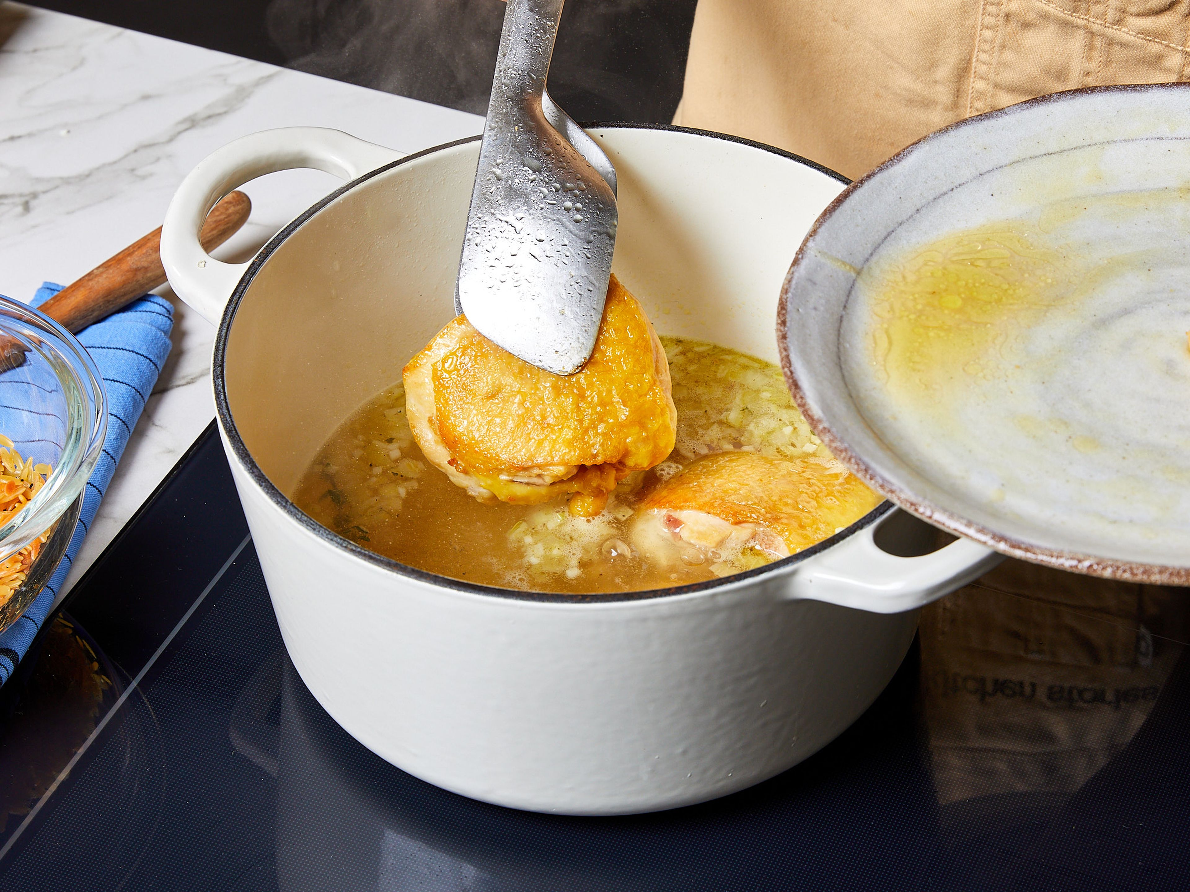 Die Hitze reduzieren. Zwiebel und Knoblauch in den Topf geben und ca. 1 Min. anschwitzen. Mit Hühnerbrühe ablöschen, Lorbeerblatt und Thymian hinzufügen und mit Salz und Pfeffer würzen. Die Flüssigkeit aufkochen lassen, dann das Hähnchen wieder hinzufügen und zugedeckt  für ca. 15–20 Min. köcheln lassen, bis das Hähnchen durchgegart ist. Hähnchen herausnehmen und Orzo in die Brühe geben. Bei niedriger Hitze ca. 15–18 Min. köcheln lassen, dabei gelegentlich umrühren.