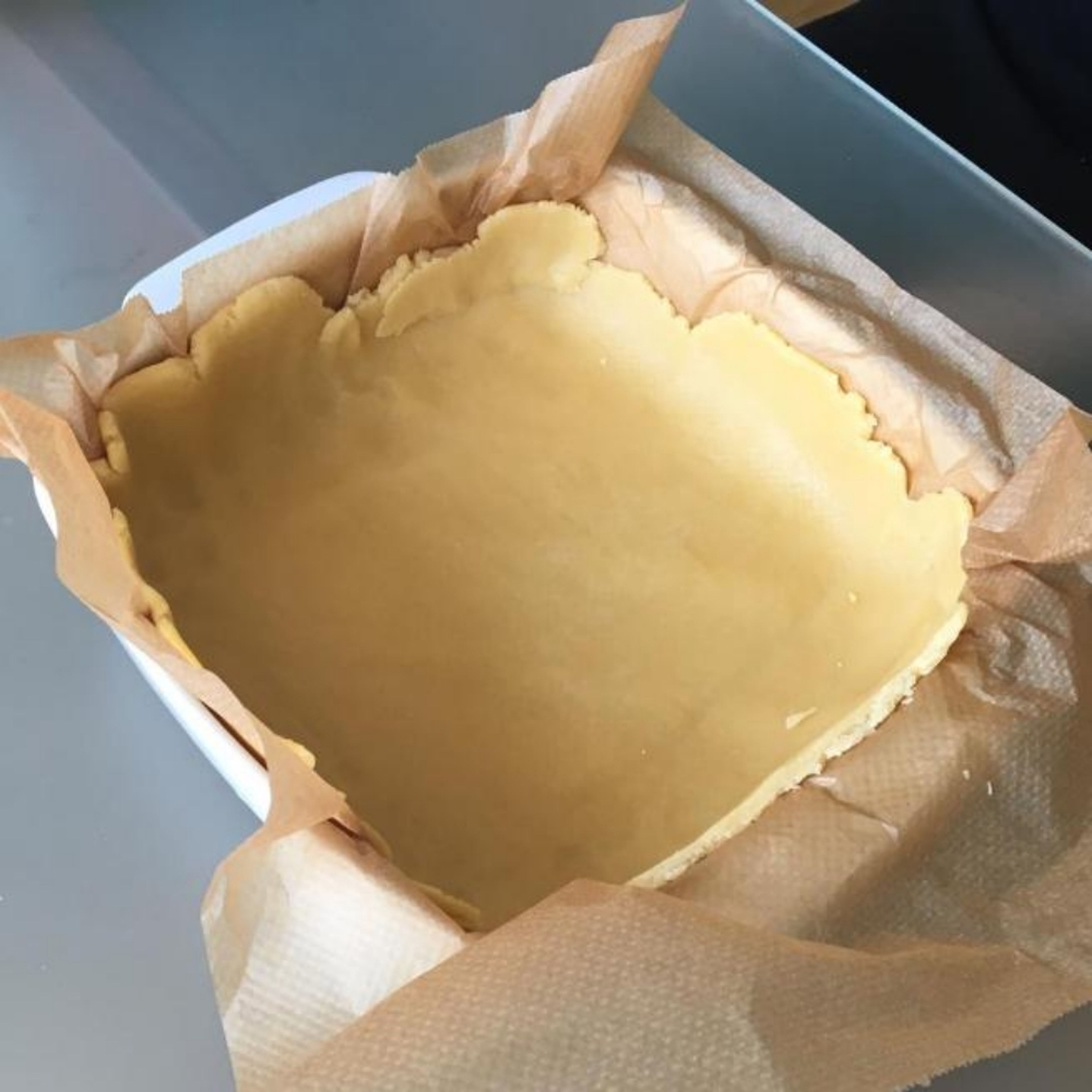 Take the dough from the fridge and put it into a baking pan keeping the baking paper underneath. Remove the dough in excess from the sides and save it for the stripes.