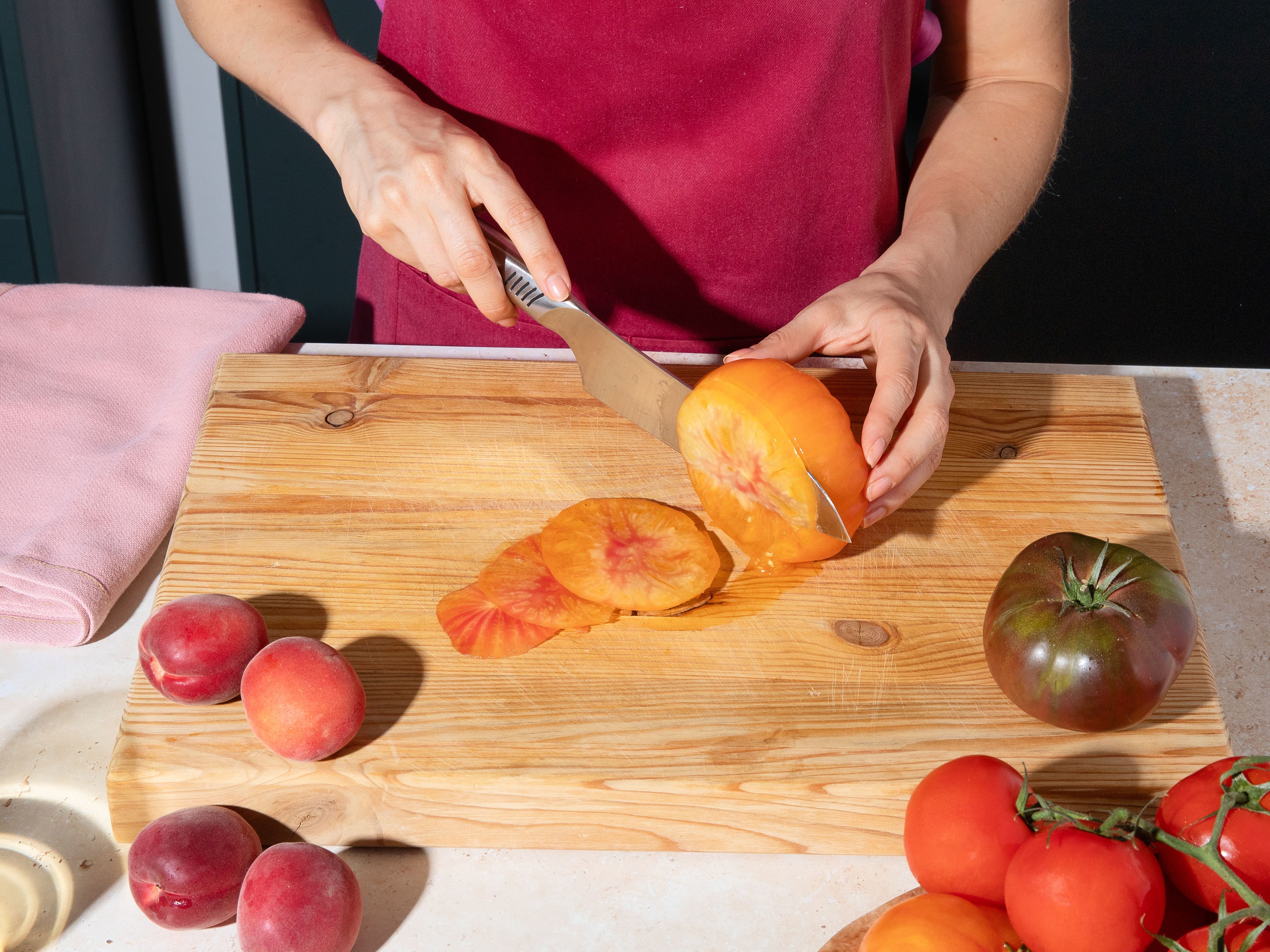 Tomaten mit einem scharfen Messer in sehr dünne Scheiben schneiden. Auf Küchenpapier auslegen, leicht salzen und etwas ziehen lassen. Danach den austretenden Saft ggf. vorsichtig abtupfen. Währenddessen Aprikosen vom Stein befreien und ebenfalls in dünne Scheiben schneiden.